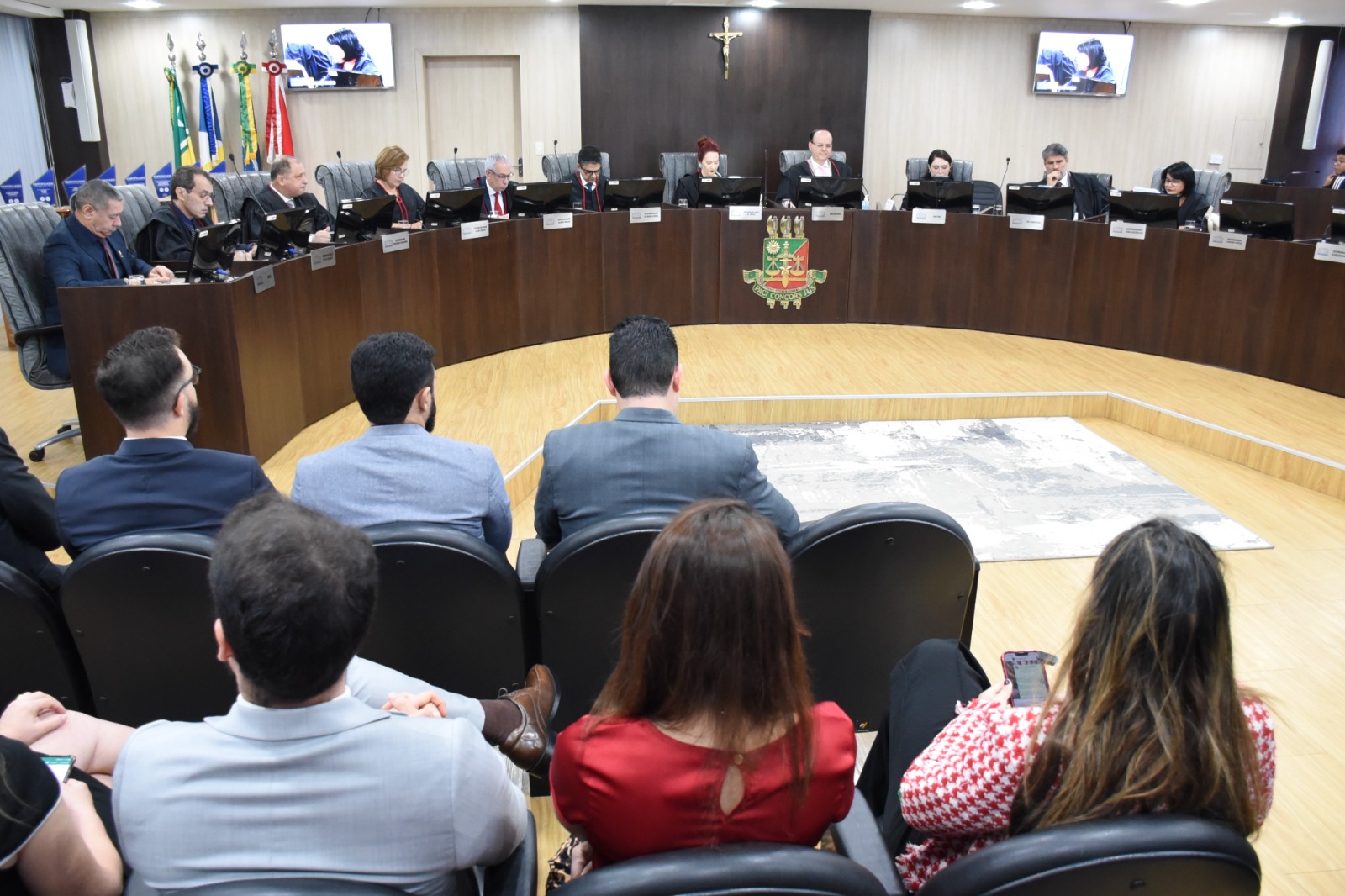 Imagem  colorida em formato retangular mostra a Sala de Sessões do Pleno, no Palácio da Justiça, durante uma cerimônia conduzida pelo presidente do TJRR, desembargador Cristóvão Suter, a imagem mostra a bancada do pleno ocupada por 11 magistrados e magistradas  do poder público, a frente da bancada estar uma plateia composta por homens e mulheres.