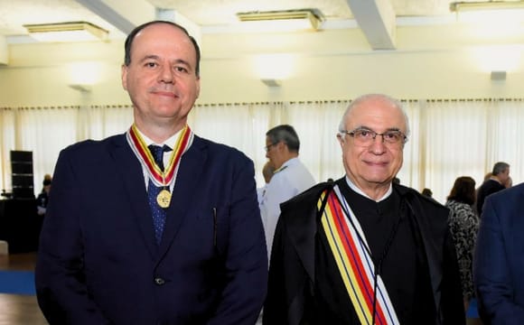 Imagem colorida diretor da Escola do Poder Judiciário de Roraima (EJURR), desembargador Cristóvão Suter com uma medalha de ouro de honra ao mérito em seu pescoço, ao seu lado com uma faixa nas cores branco,vermelho e amarelas está o presidente do Superior Tribunal Militar (STM), ministro Tenente Brigadeiro do Ar, Francisco Joseli Parente Camelo.