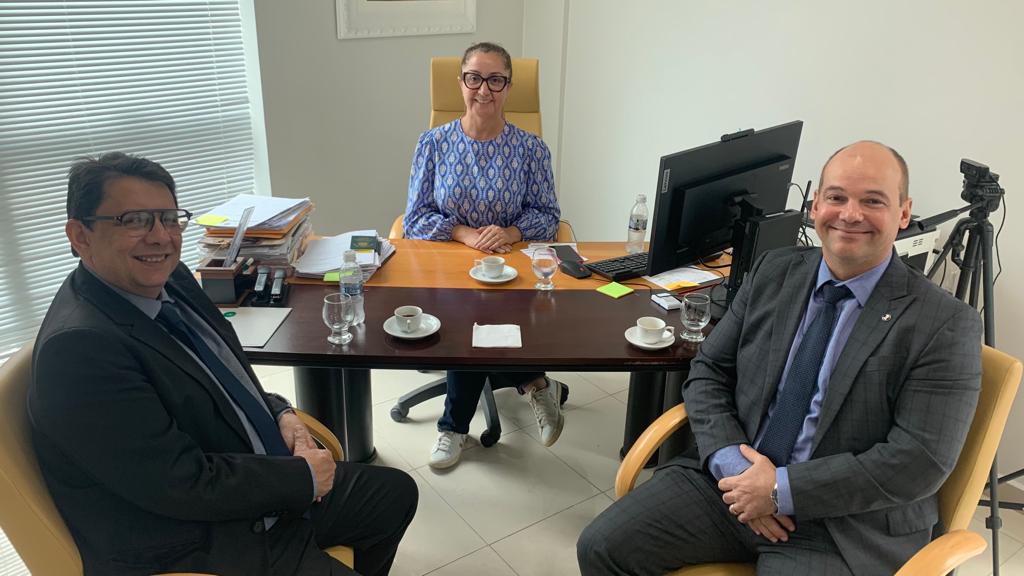  Imagem colorida mostra o presidente do Tribunal de Justiça de Roraima (TJRR), desembargador Jésus Nascimento acompanhado do juiz Eduardo Álvares de Carvalho, coordenador Natjus e do Comitê Estadual de Saúde a frente de uma mesa sentados em lados opostos  olhando para câmera. no centro atrás da mesa , também olhando para a foto está a presidente do Conselho Regional de Medicina em Roraima (CRM), Blenda Avelino Garcia.