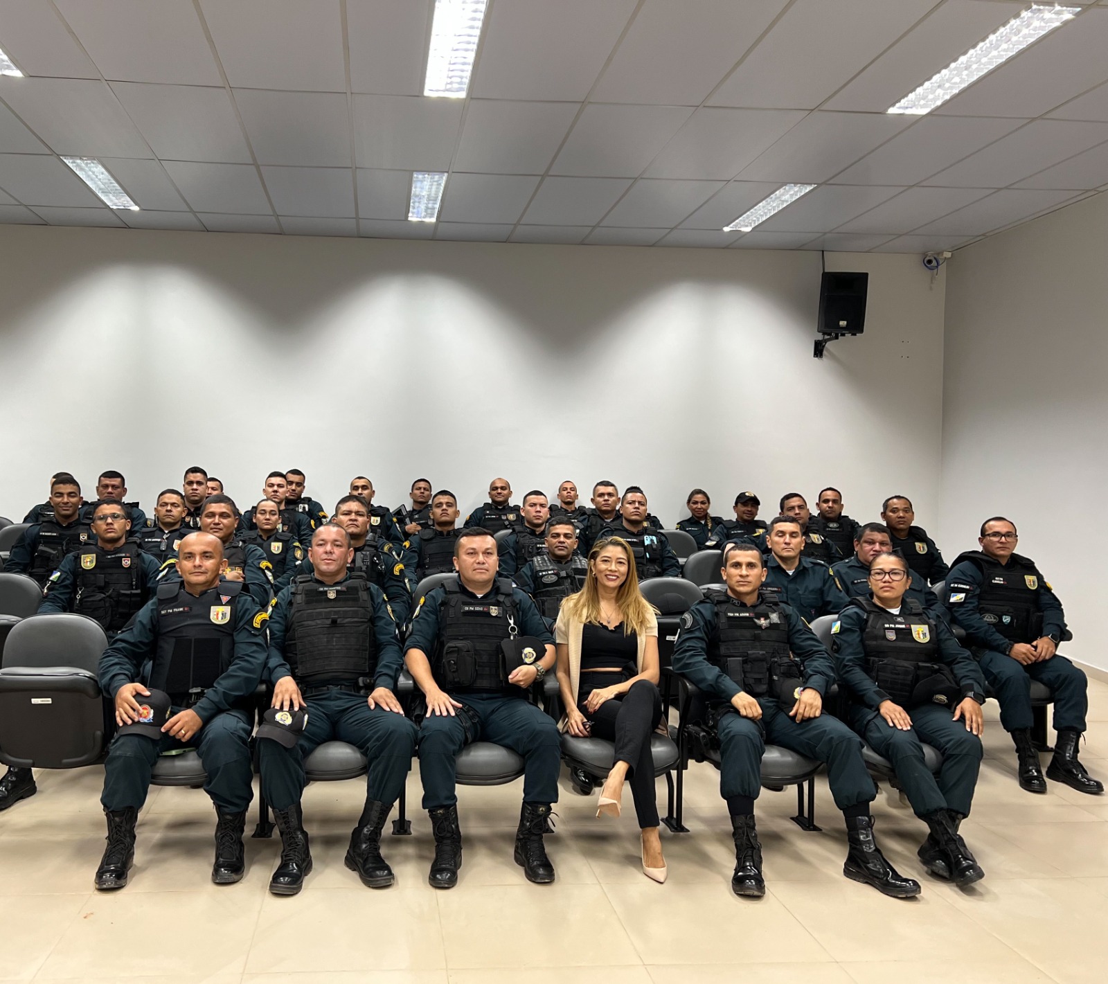 FOTO COLORIDA DA SERVIDORA E DOS POLICIAS SENTADAS E OLHANDO PARA A FOTOGRAFIA