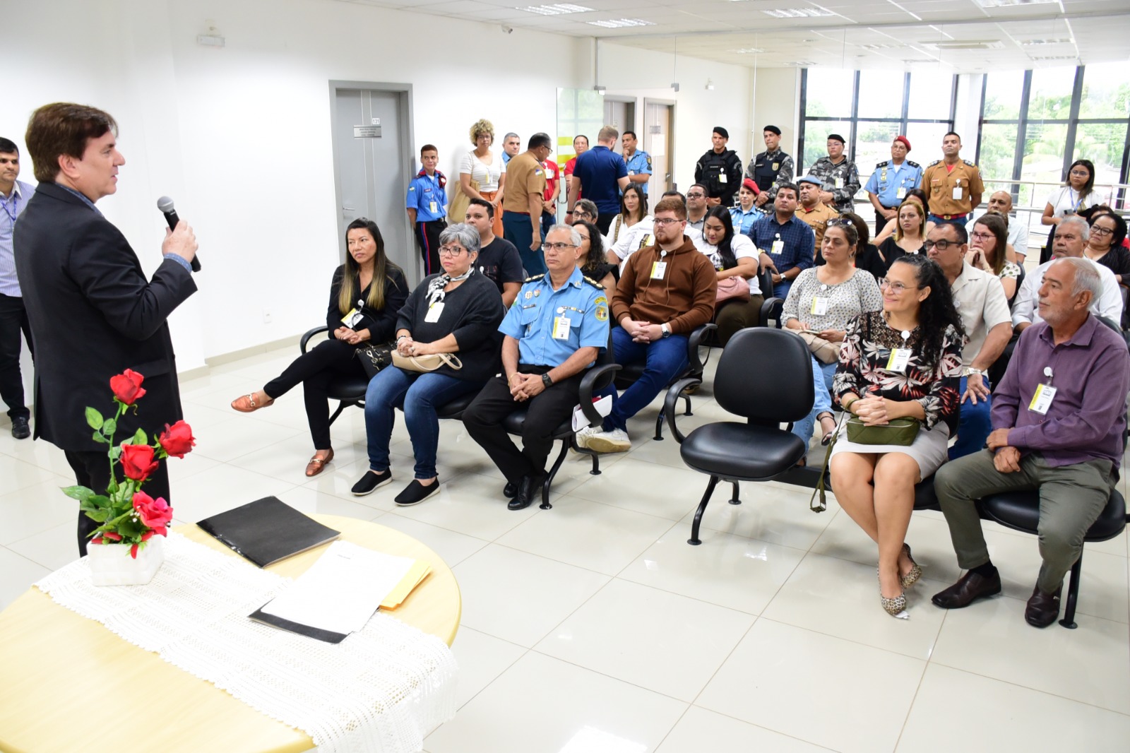 foto colorida de uma sala com servidores sentados em cadeiras pretas e afrente há um homem  falando ao microfone