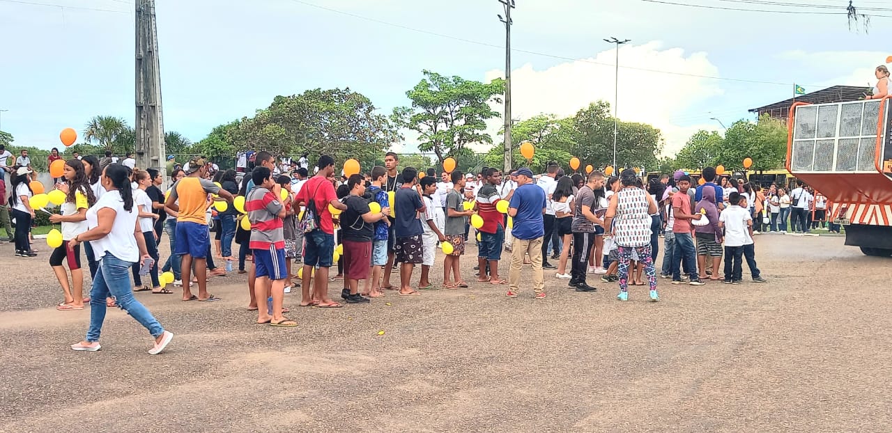  Imagem colorida mostra um aglomerado de pessoas reunidas segurando balões amarelos. 