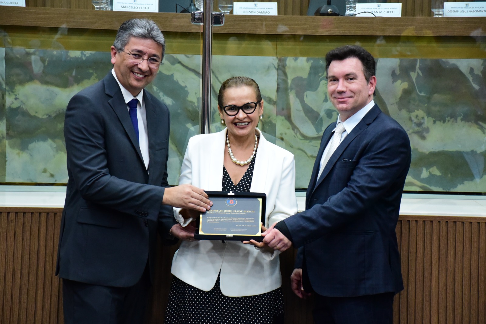 foto colorida de uma homenagiada sendo premiada e pousando para a foto junto com mais duas autoridades