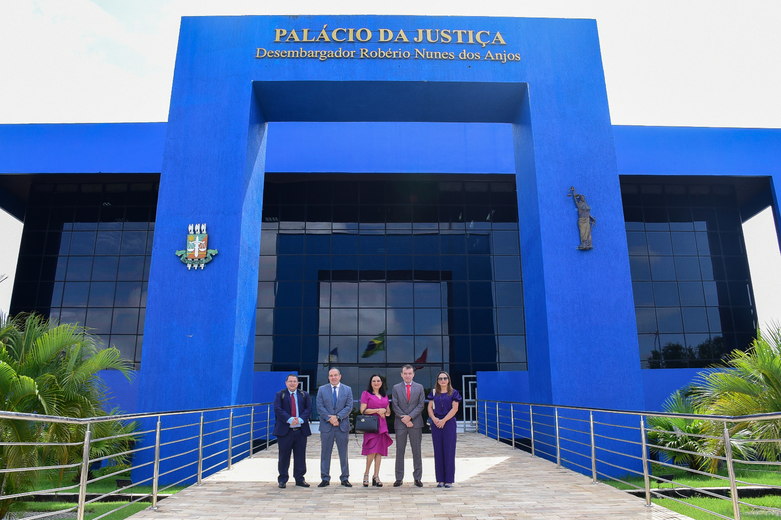 FOTO COLORIDA DE CINCO PESSOAS DA COMITIVA POUSANDO PARA A FOTO ENFRENTE AO PALÁCIO