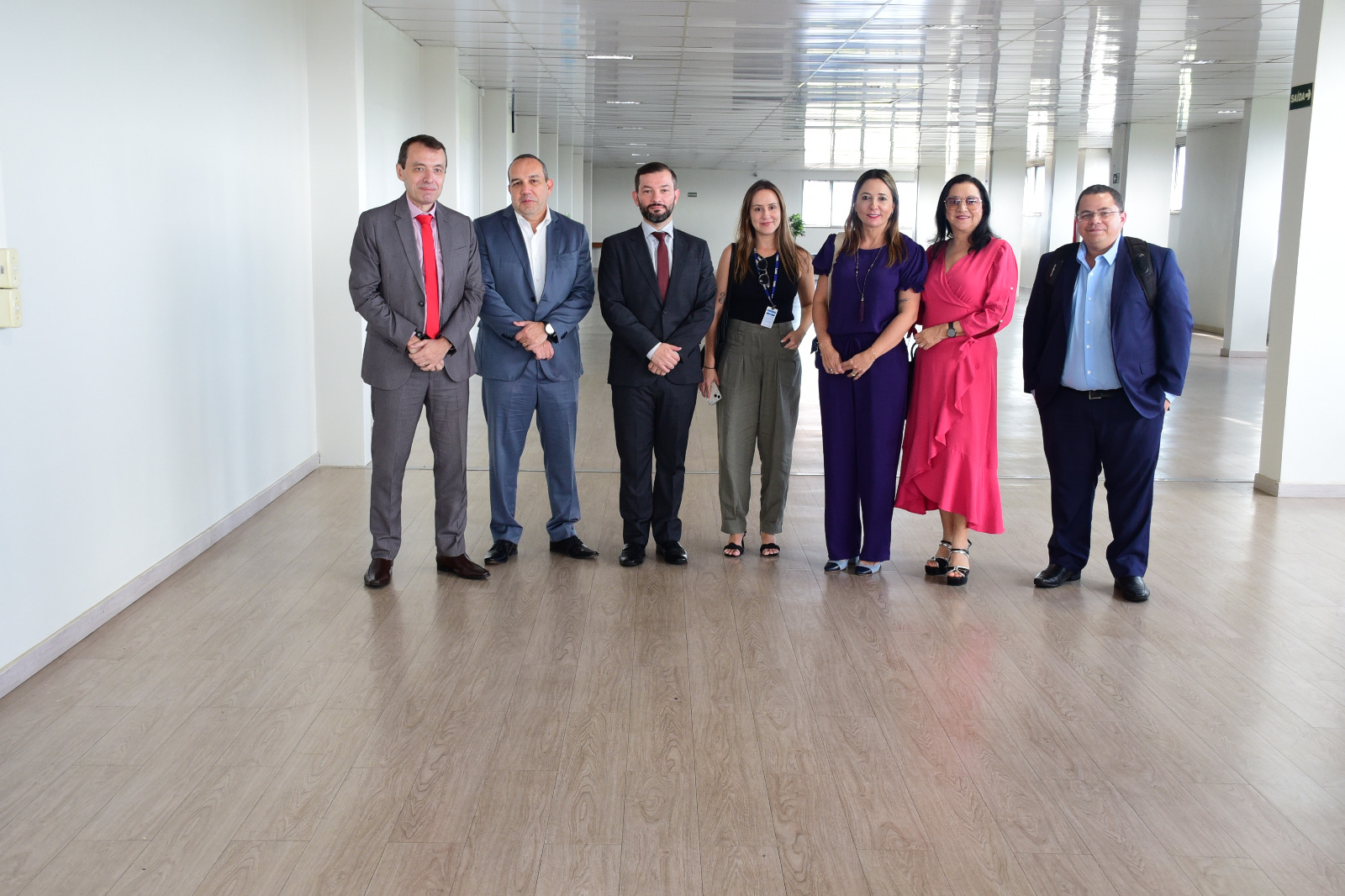 FOTO COLORIDA DE SETE PESSOAS DENTRE ELAS SERVIDORES E DA COMITIVA EM PÉ POUSANDO PARA A FOTO