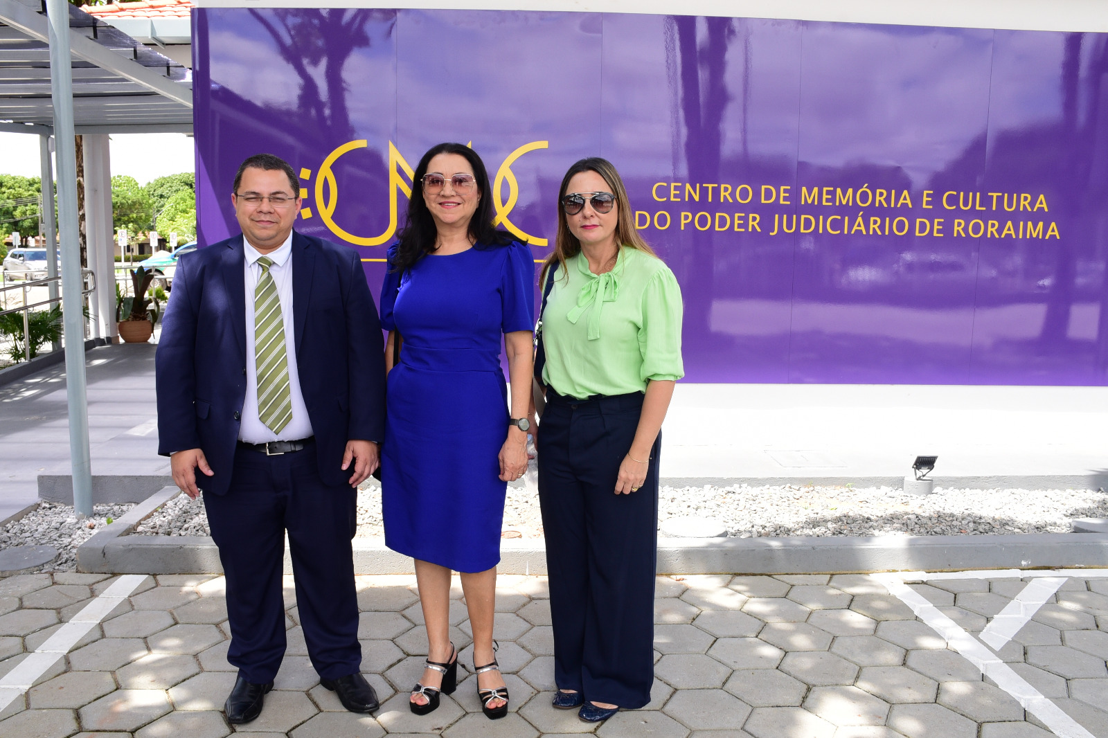FOTO COLORIDA DE  TREZ PESSOA DA COMITIVA ENFRENTE AO CMC