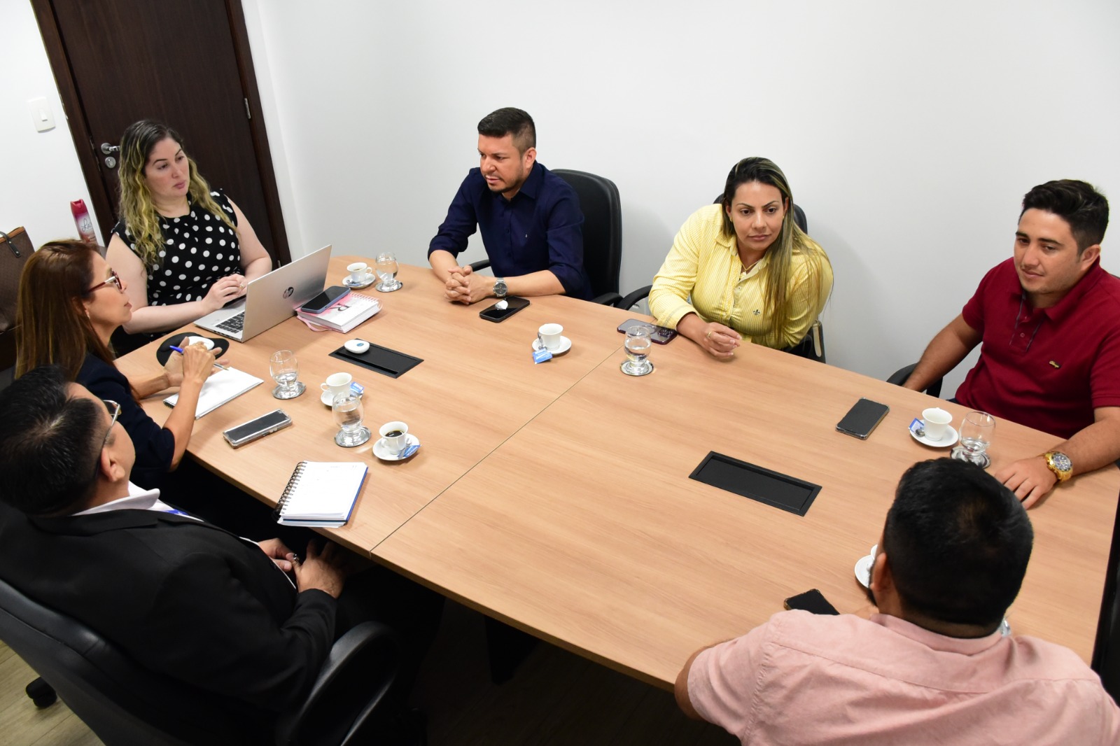 foto colorida de sete pessoas em reunião ao redor de uma mesa amadeirada
