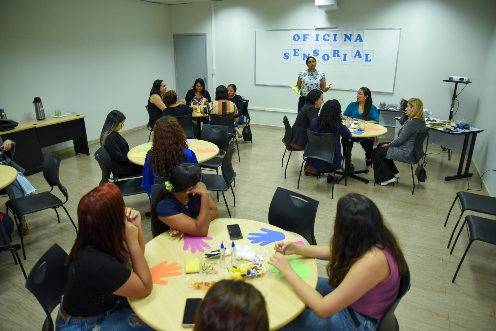 FOTO COLORIDA DE UMA SALA DE AULA COM AS PESSOAS SENTADAS EM CADEIRAS ESCOLARES