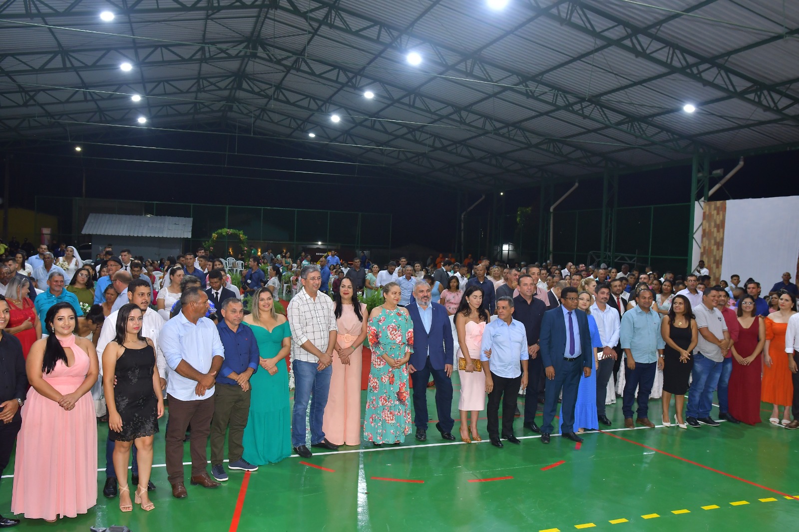 foto colorida mostra os noivos e convidados do casamento coletivo da Justiça Itinerante do TJRR, posando para fotografia. No plano de fundo se encontram outras pessoas que participaram da cerimônia matrimonial.