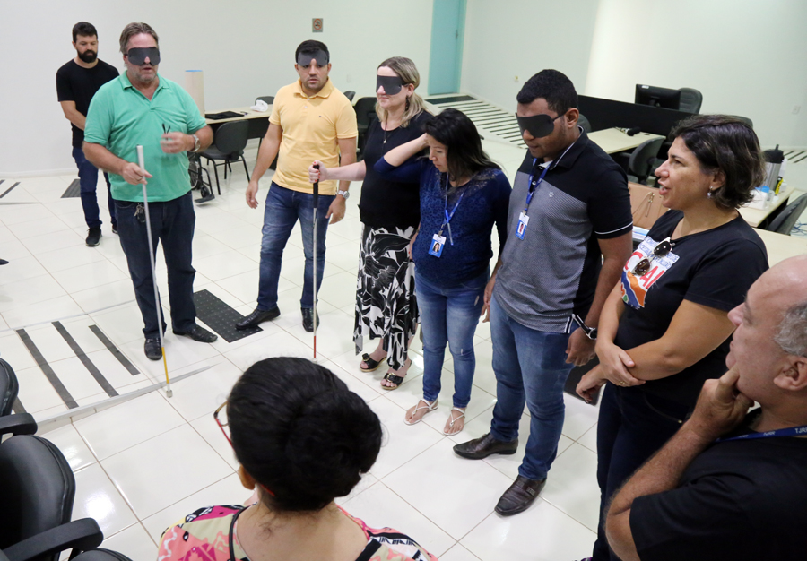 foto colorida de u,a roda com serviores realizando uma dinamica sobre cegueira, eles estão segurando um bastão e estão com olhos vendados  