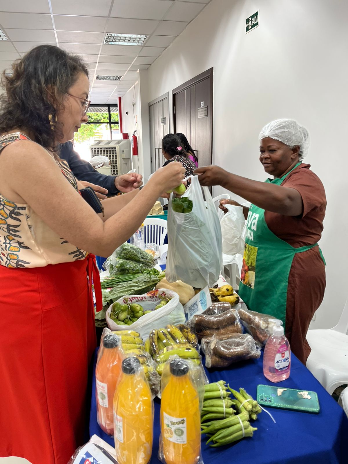 foto colorida de uma feira orgânica organizada dentro do TJRR nela há uma feirante vendendo e uma servidora comprando