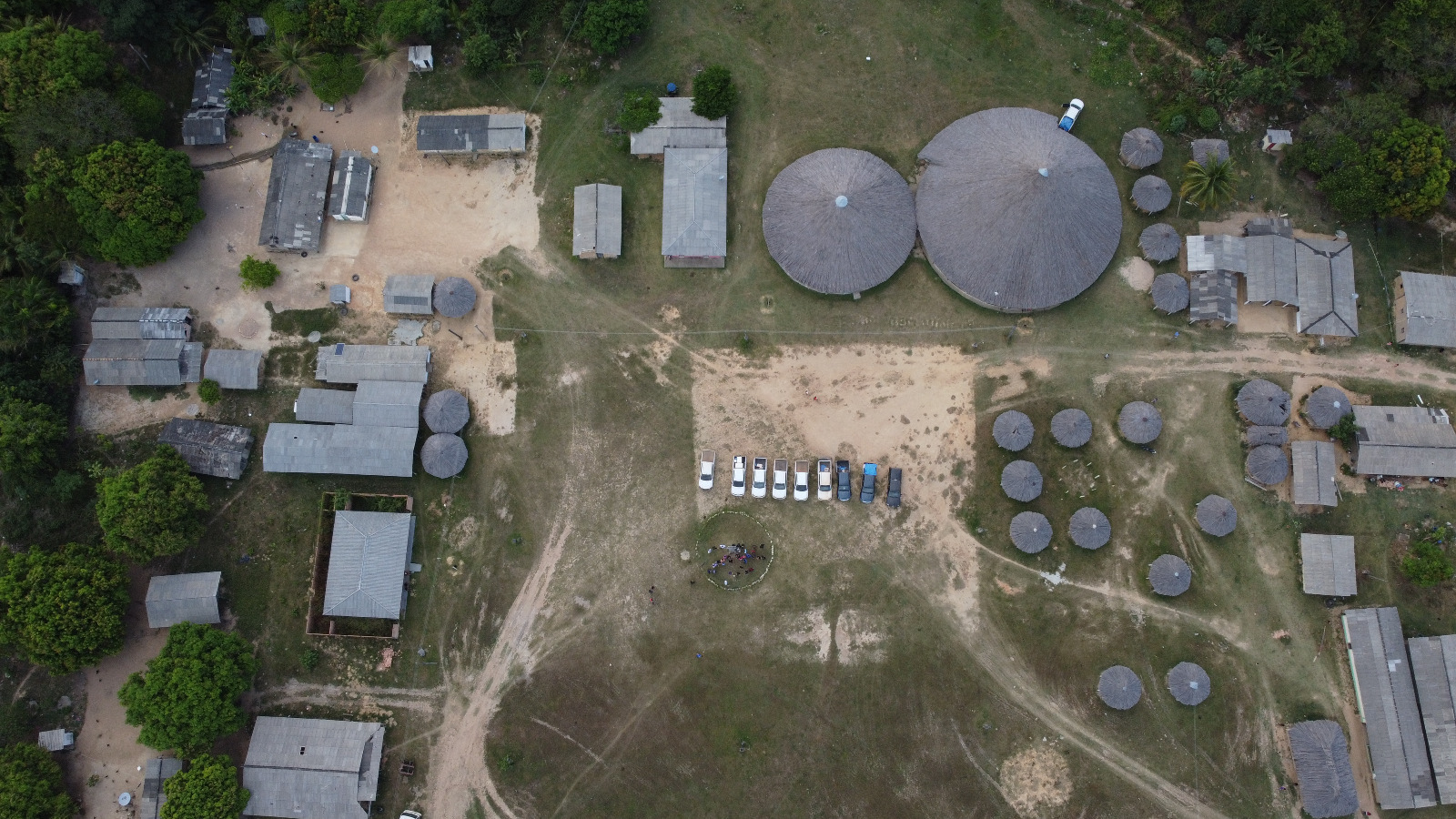  foto colorida tirada por drone da parte de cima da comunidade indigena. Na área mostra uma comunidade composta por malocas e barracões, há também estacionados perto da roda de conversa nove carros da  A Coordenadoria de Violência Doméstica do Tribunal de Justiça de Roraima