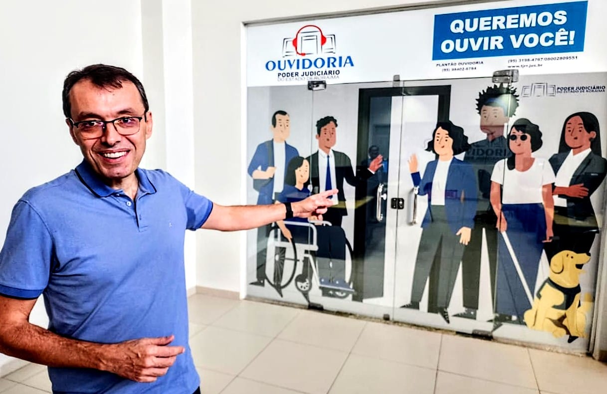 Imagem colorida mostra o desembargador Erick Linhares, Ouvidor-Geral do TJRR, sinalizando a entrada da Ouvidoria-Geral do Judiciário de Roraima