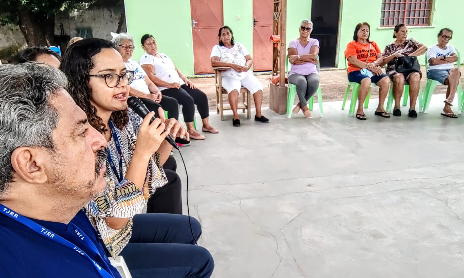 Imagem colorida mostra um grupo de onze pessoas reunidas em volta de uma roda de conversa. Na imagem uma mulher fala no microfone. 