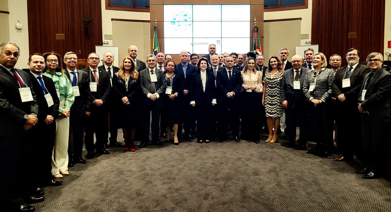 A imagem colorida contém os ouvidores judiciais do país reunidos posando para fotografia, durante o IX Encontro do Colégio Nacional de Ouvidores Judiciais - COJUD, enquanto um ouvidor está palestran