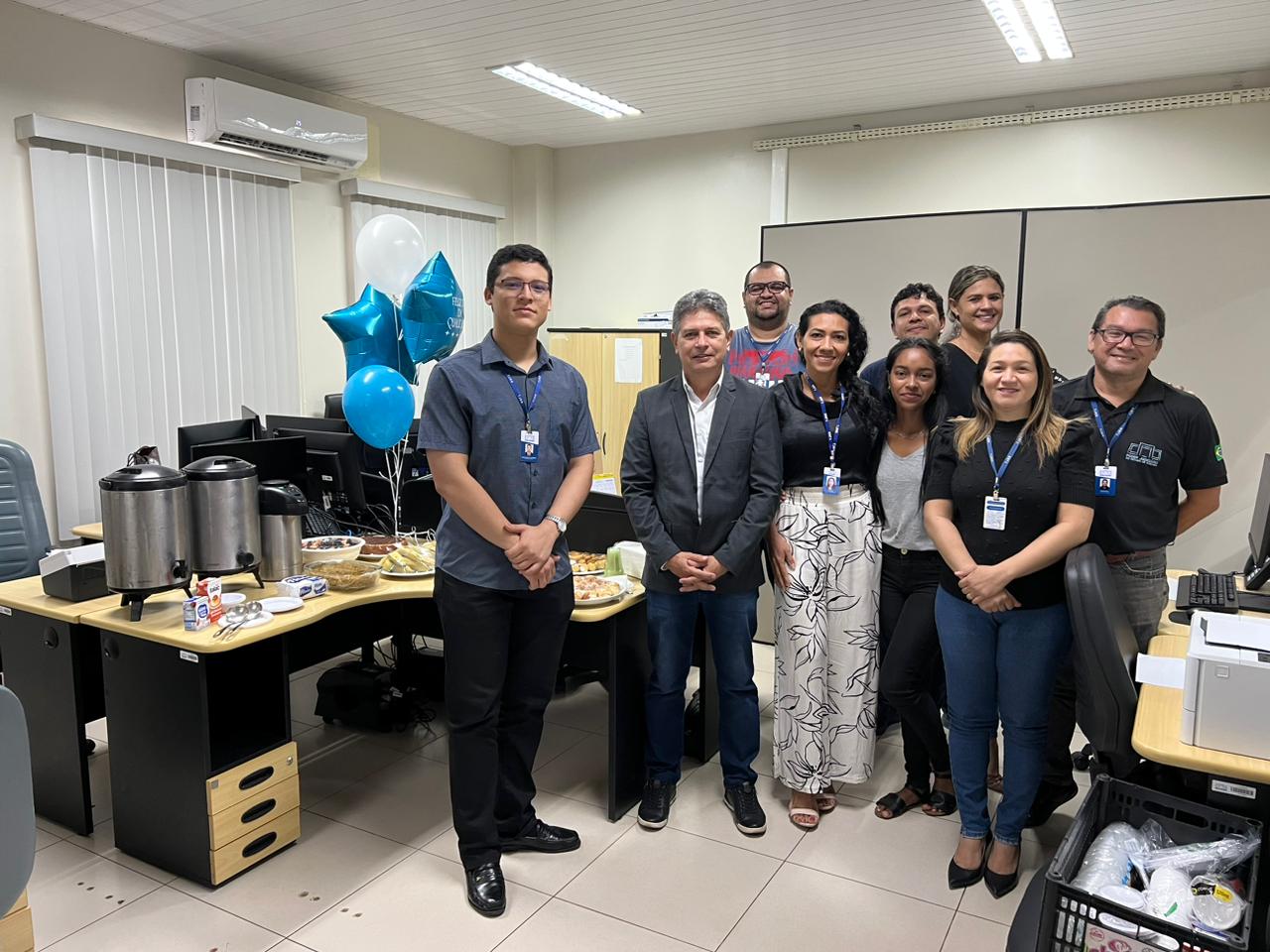 foto colorida de servidores do Tjrr pousando para a foto e ao meio há um carrinho de metal com o lanche e balões azul e branco pendurado  