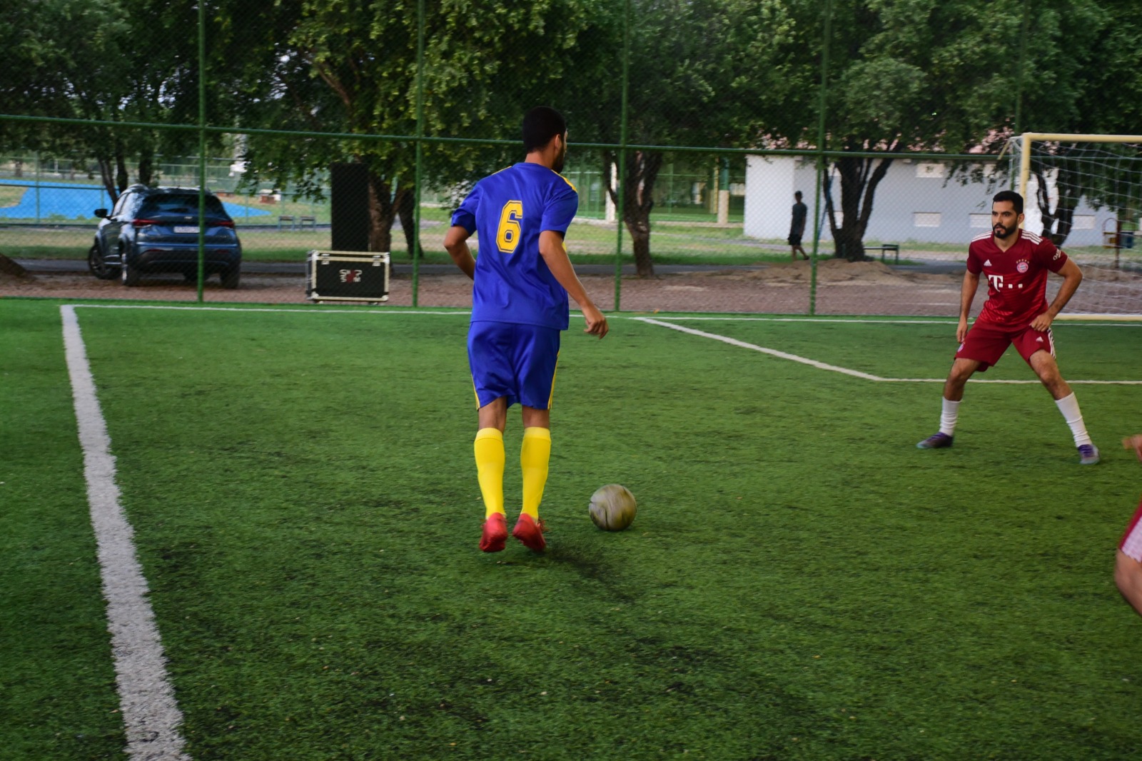  imagem colorida mostra dois jogadores de times adversários, um do time azul tentando driblar um jogador do time vermelho.