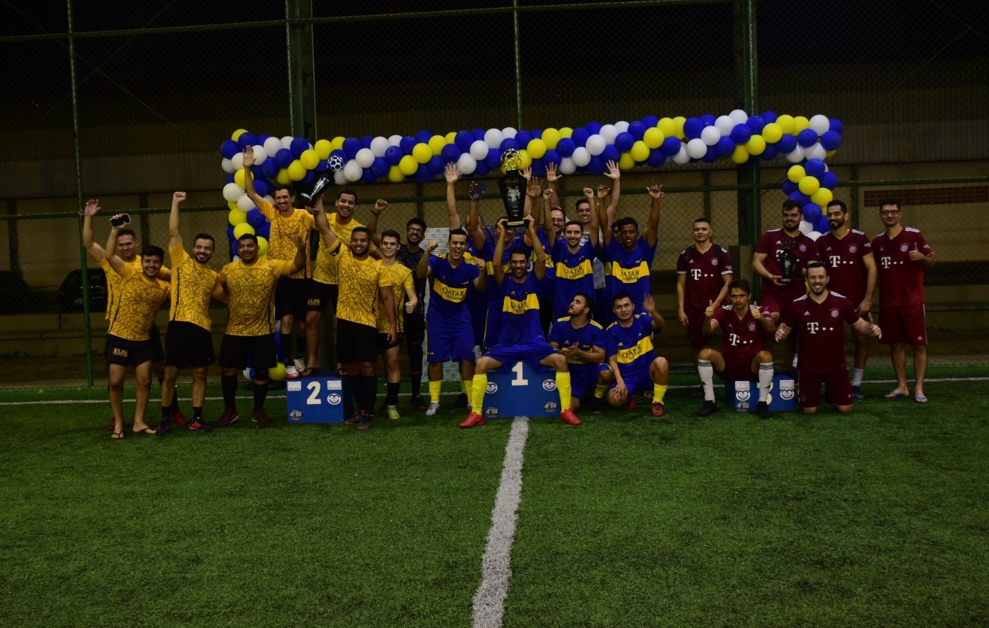 magem colorida mostra uma dupla de jogadores do time amarelo, batendo as mãos em comemoração após terem feito gol. 
