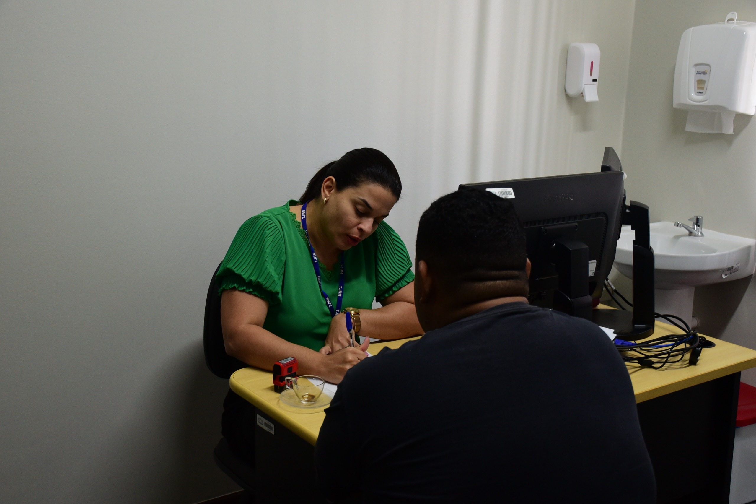  foto colorida de uma servidora do TJRR realizando a aviação de outro servidor que está sentado à sua frente.