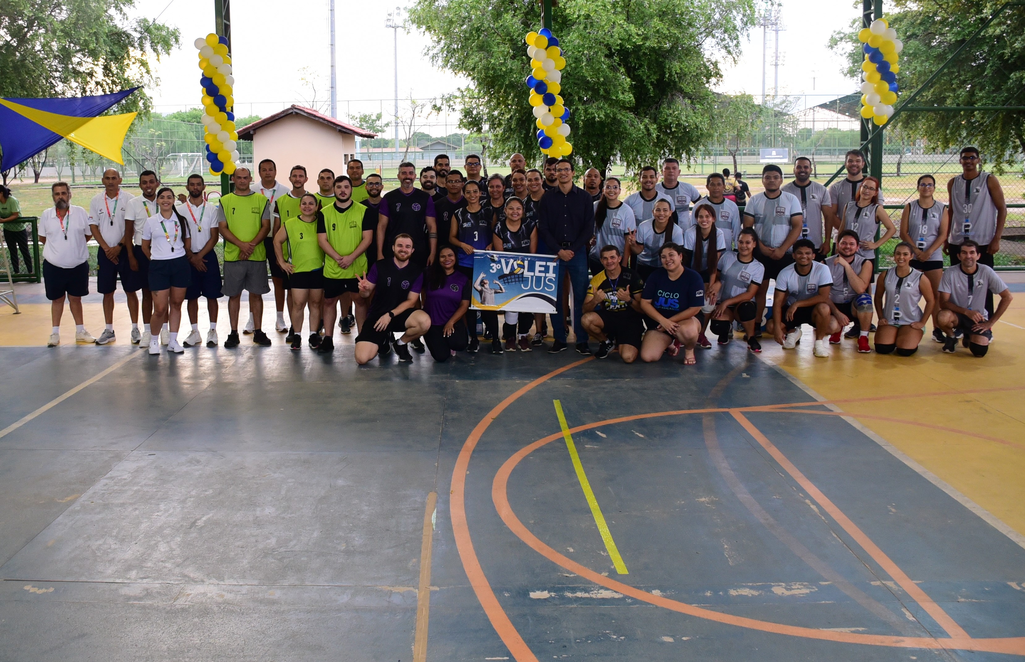  Imagem colorida de dois times em uma partida de vôlei. Um dos atletas está jogando a bola por cima da rede enquanto outro prepara o bloqueio.