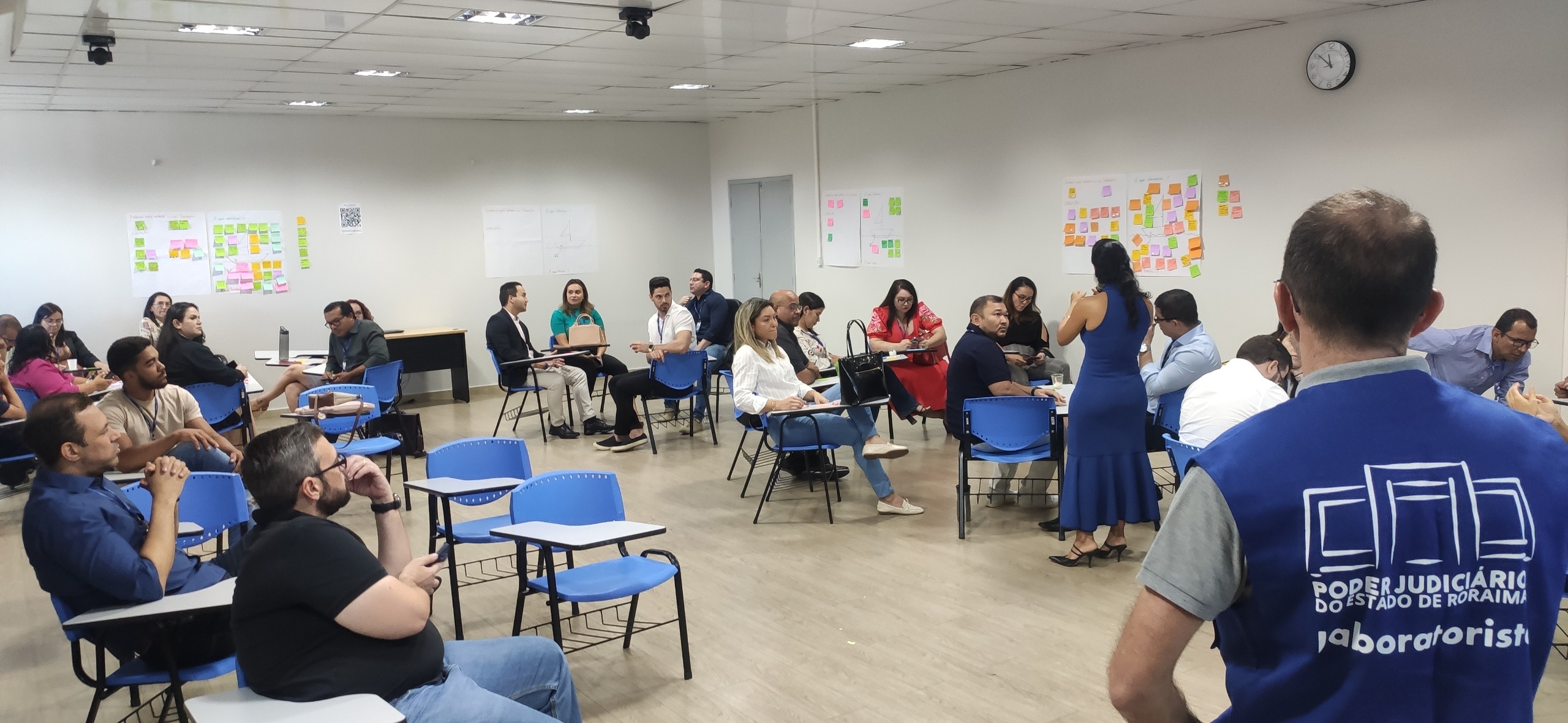 foto colorida de uma sala e servidores sentados em círculos em cadeiras de estudos azul e branco.