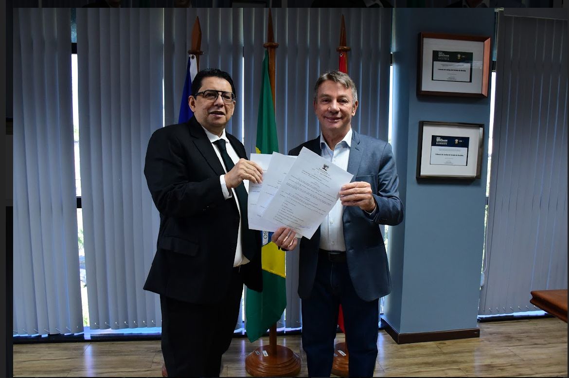 foto colorida do presidente do TJRR, desembargador Jésus Nascimento junto com o Governador Antônio denarium  pousando para a fotografia om papeis em mãos