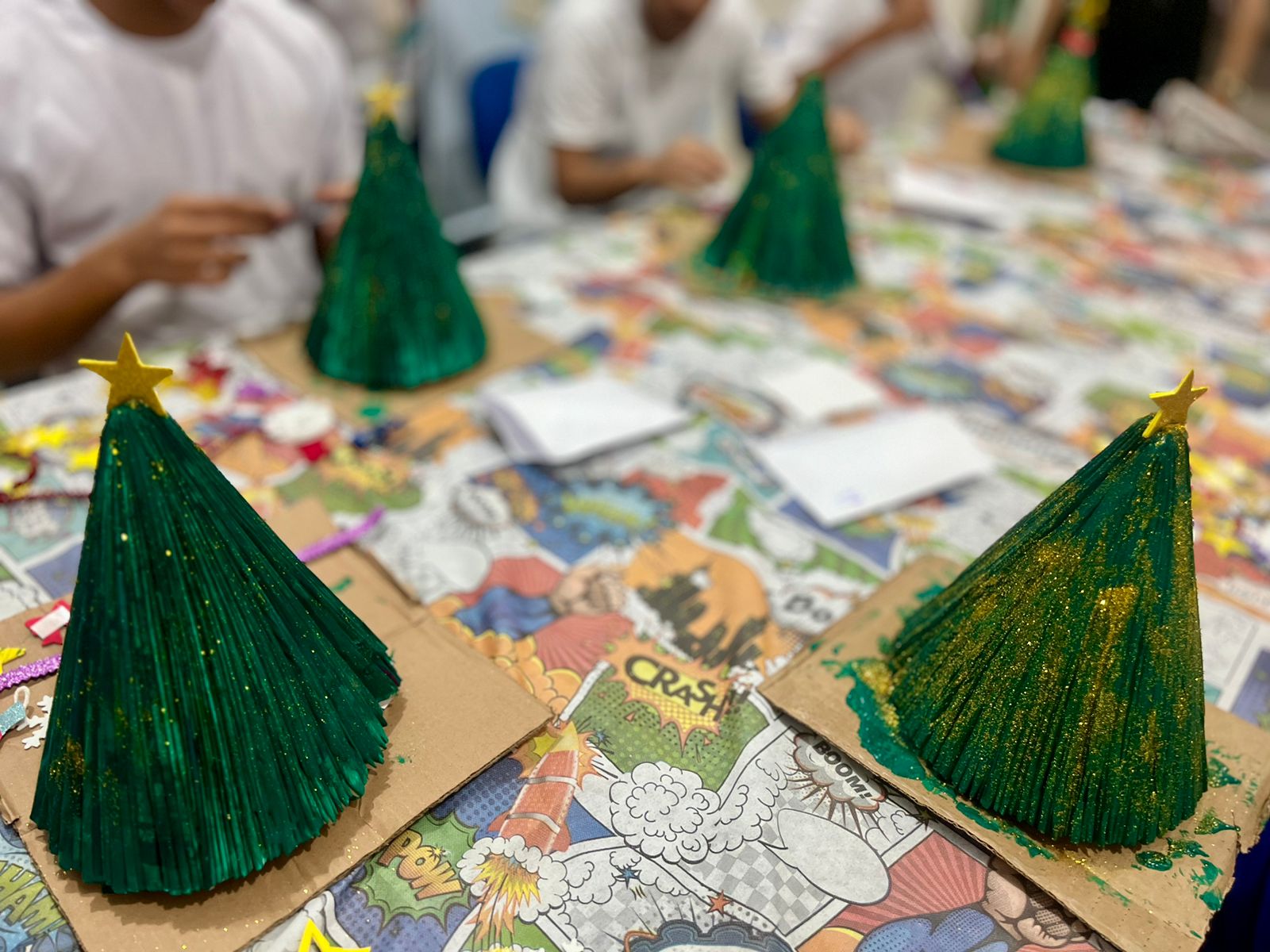 foto colorida mostra quatro mini árvores de natal sendo confeccionadas