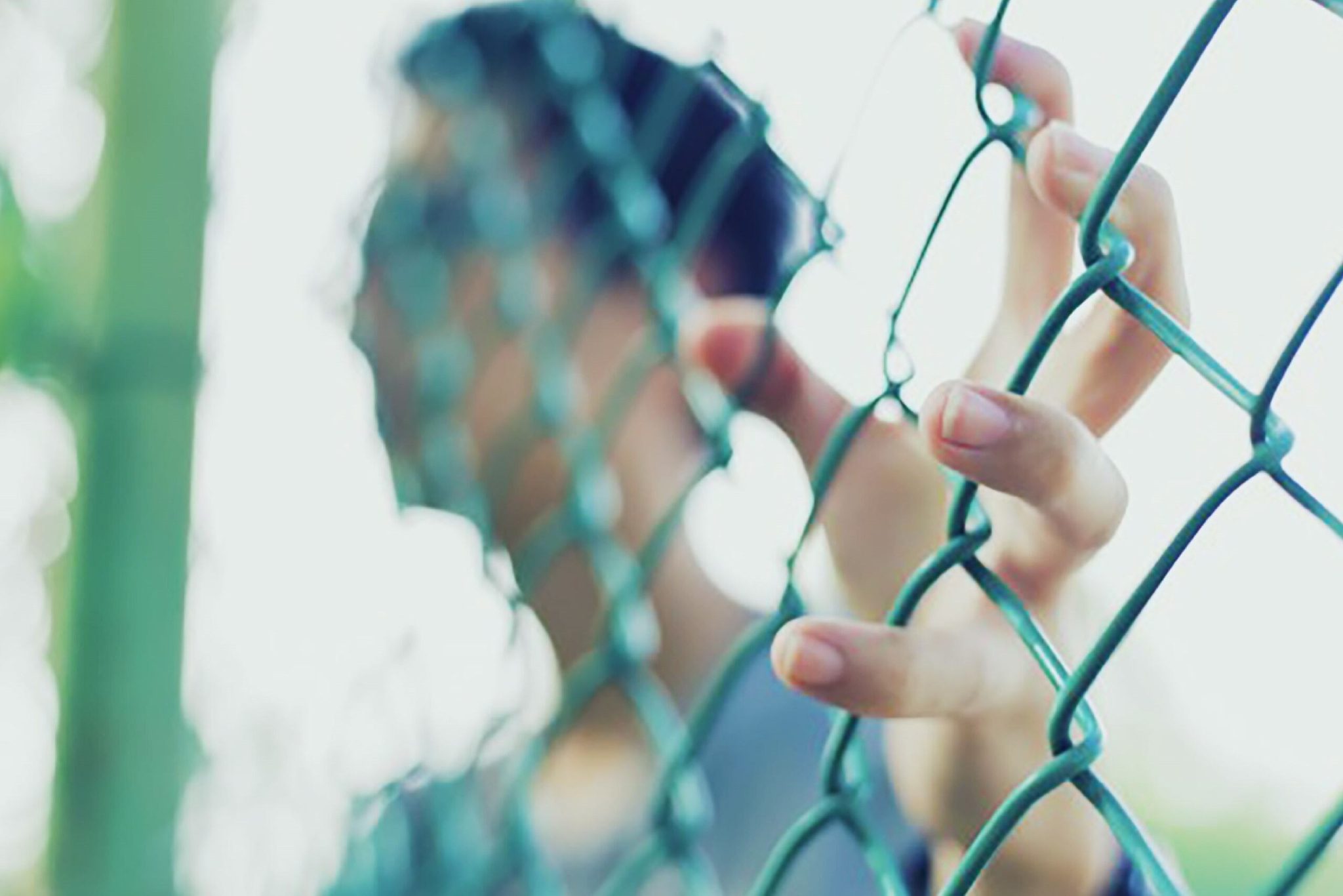 Imagem colorida mostrando um homem escorado em uma grade. A imagem está turva e não mostra a fisionomia com clareza