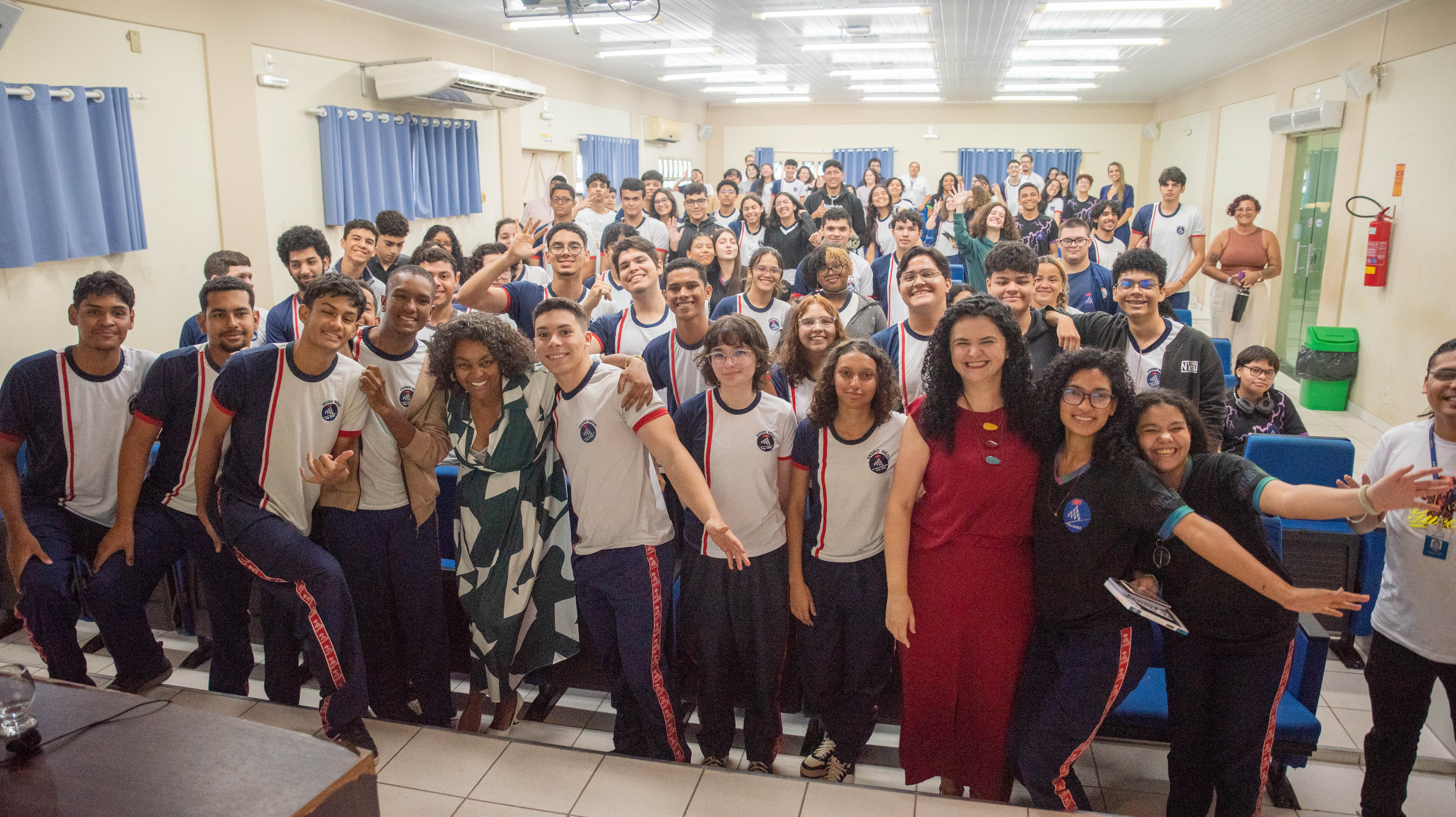 Foto colorida mostra aproximadamente 60 pessoas posando para foto em um auditório. entre elas, estudantes, professores, servidores do TJRR e a palestrante 