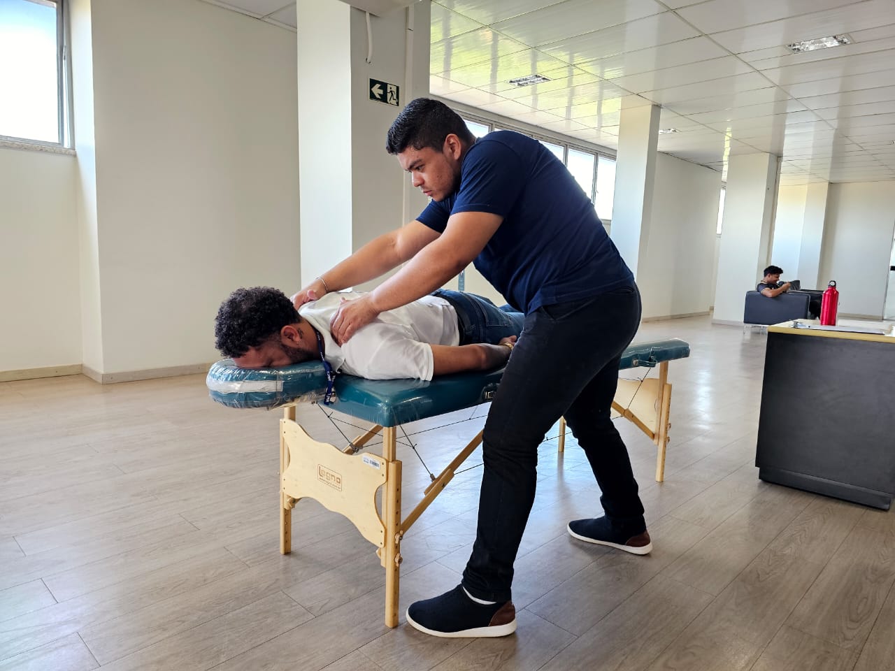 Foto colorida mostrando um homem deitado  em uma maca enquanto recebe massagem em seus ombros.