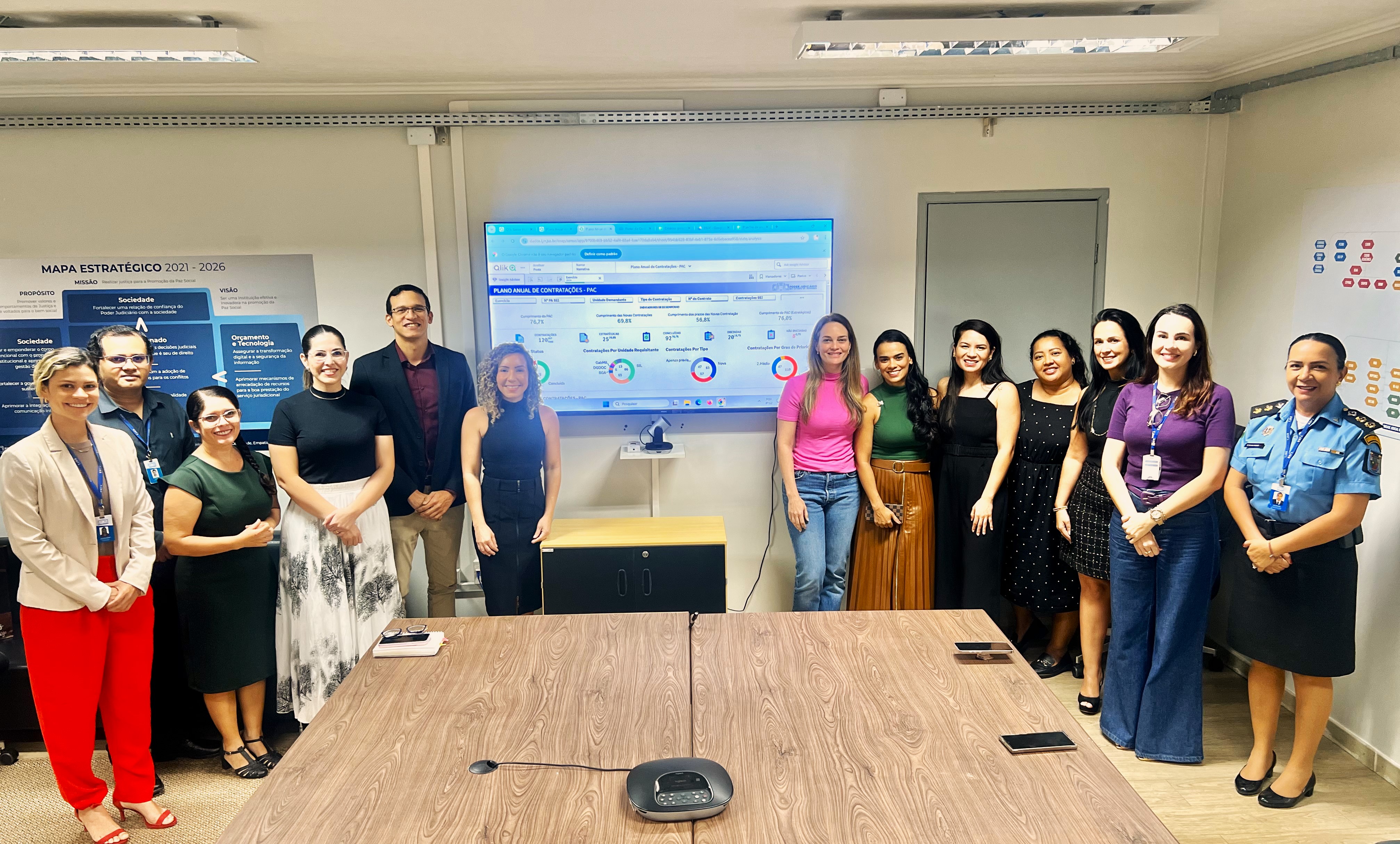 foto colorida de servidores reunidos e pousando para fotografia ao lado de uma televisão
