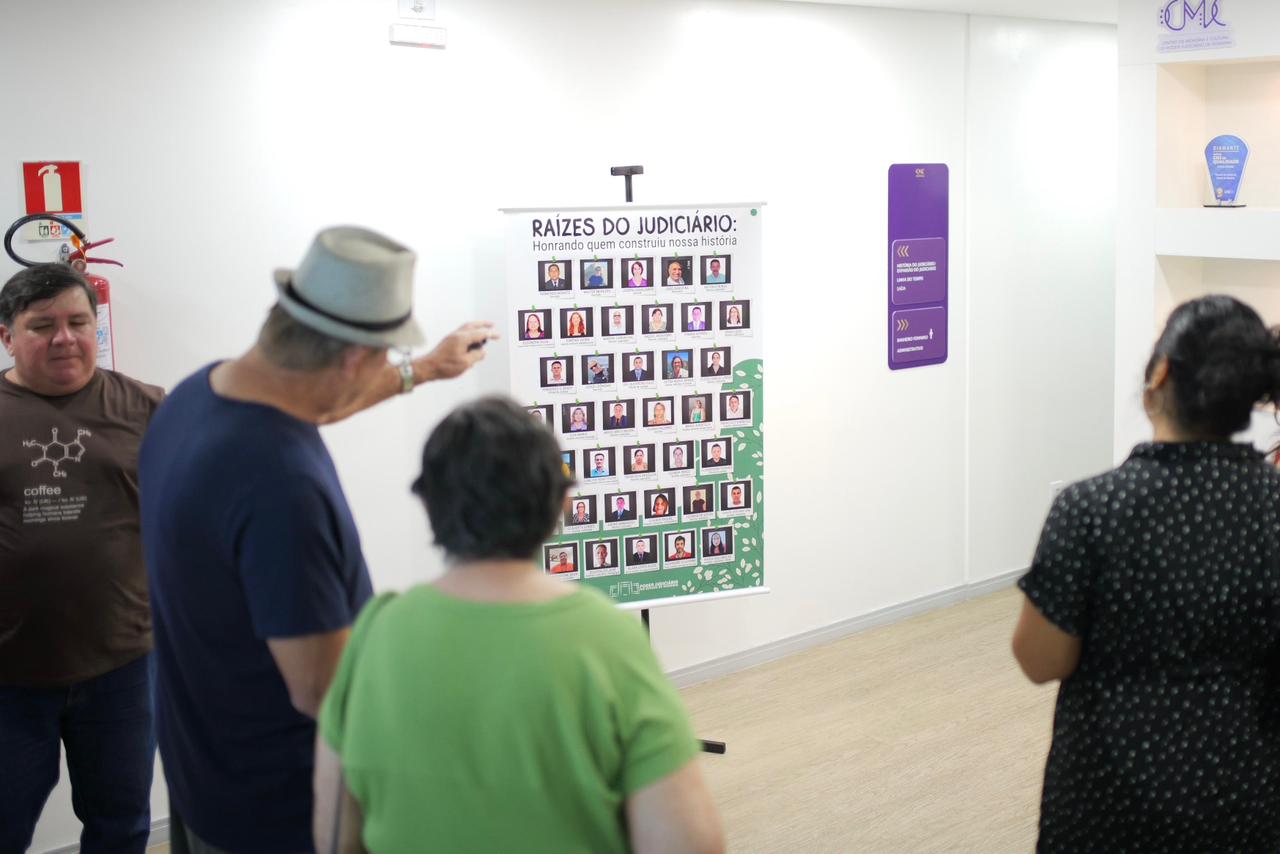 imagem colorida mostra quatro pessoas apreciando banner com fotografias de servidores e servidores do TJRR aposentados.