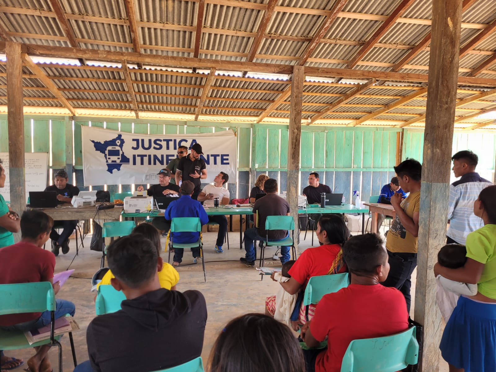 Foto colorida mostrando pessoas sendo atendidas pelos servidores da justiça itinerante e pelos parceiros. Cada cidadão está sentado em uma mesa em frente a um dos servidores