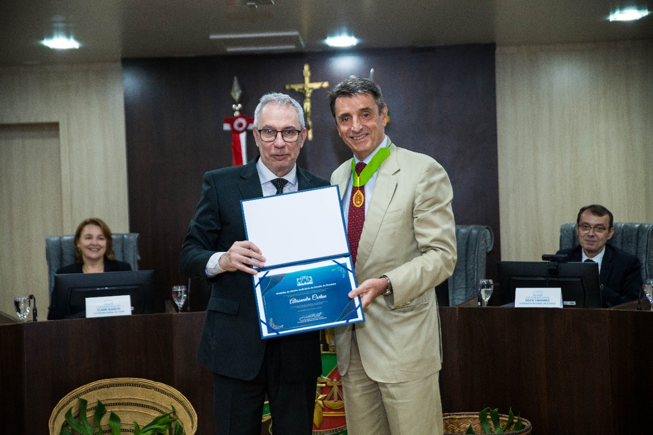Foto colorida do Alessandro Cortese pousando para fotografia ao lado Desembargador Almiro Padilha. Os dois estão segurando o diploma Foto colorida do Alessandro Cortese pousando para fotografia ao lado Desembargador Almiro Padilha. Os dois estão segurando o diploma