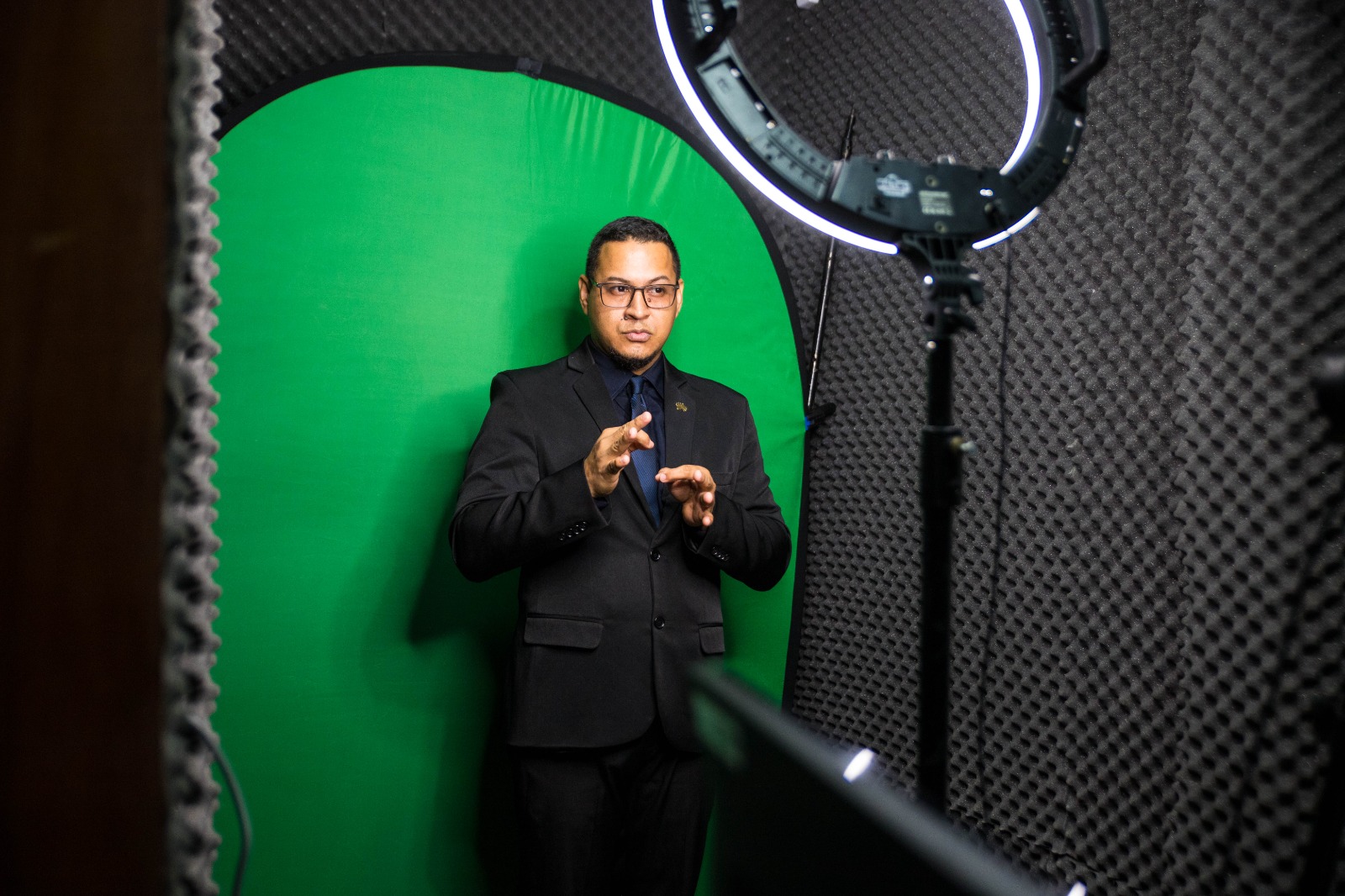 foto colorida de um intérprete de libras em um estúdio, com o fundo verde.