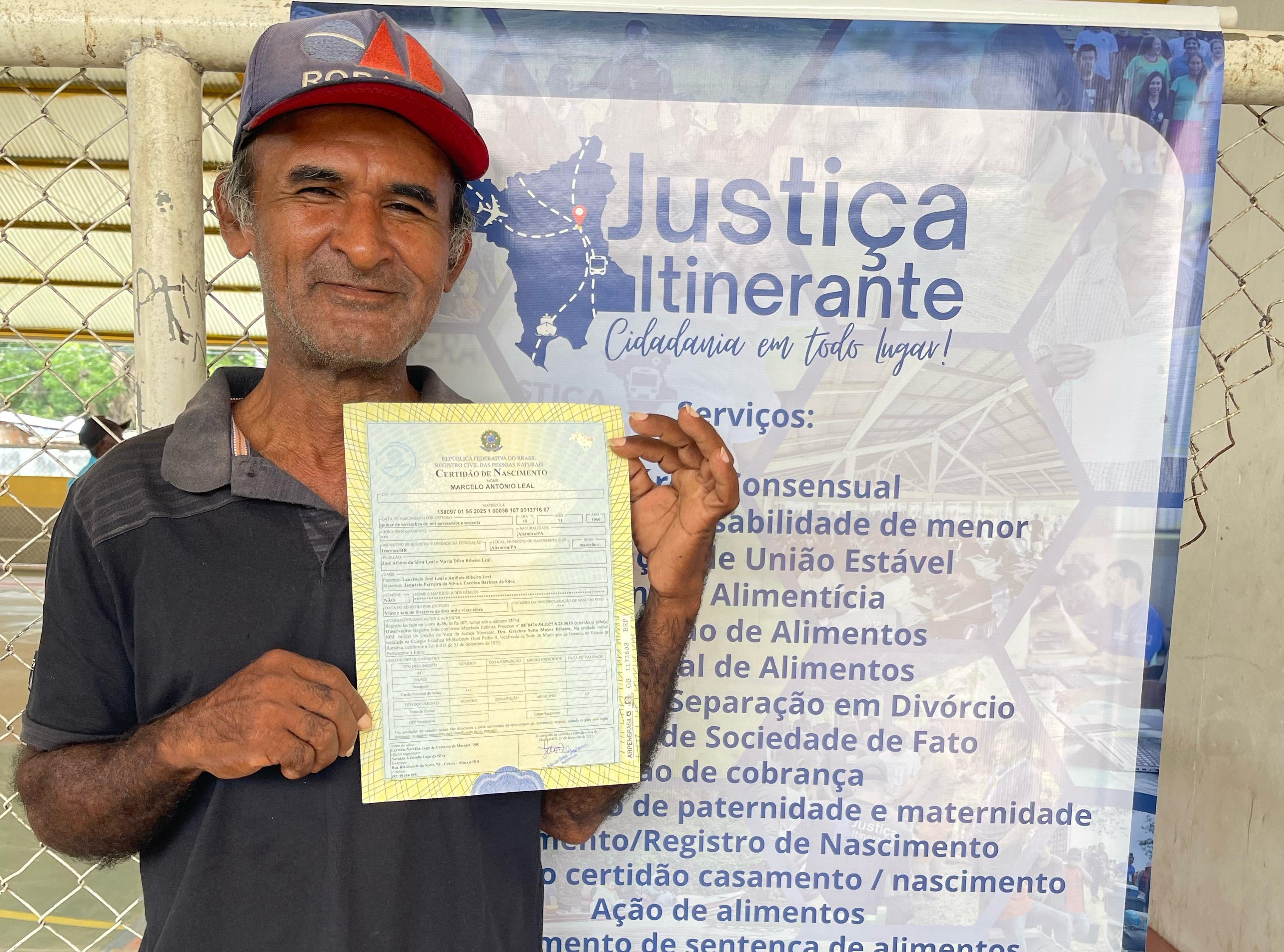 Imagem colorida contém o cidadão, Leandro Leal, atendido pela Vara da Justiça Itinerante do TJRR, segurando um certificado de nascimento. Atrás dele encontra-se um banner da Justiça Itinerante contendo os serviços da Justiça Itinerante listados. Imagem colorida contém o cidadão, Leandro Leal, atendido pela Vara da Justiça Itinerante do TJRR, segurando um certificado de nascimento. Atrás dele encontra-se um banner da Justiça Itinerante contendo os serviços da Justiça Itinerante listados.