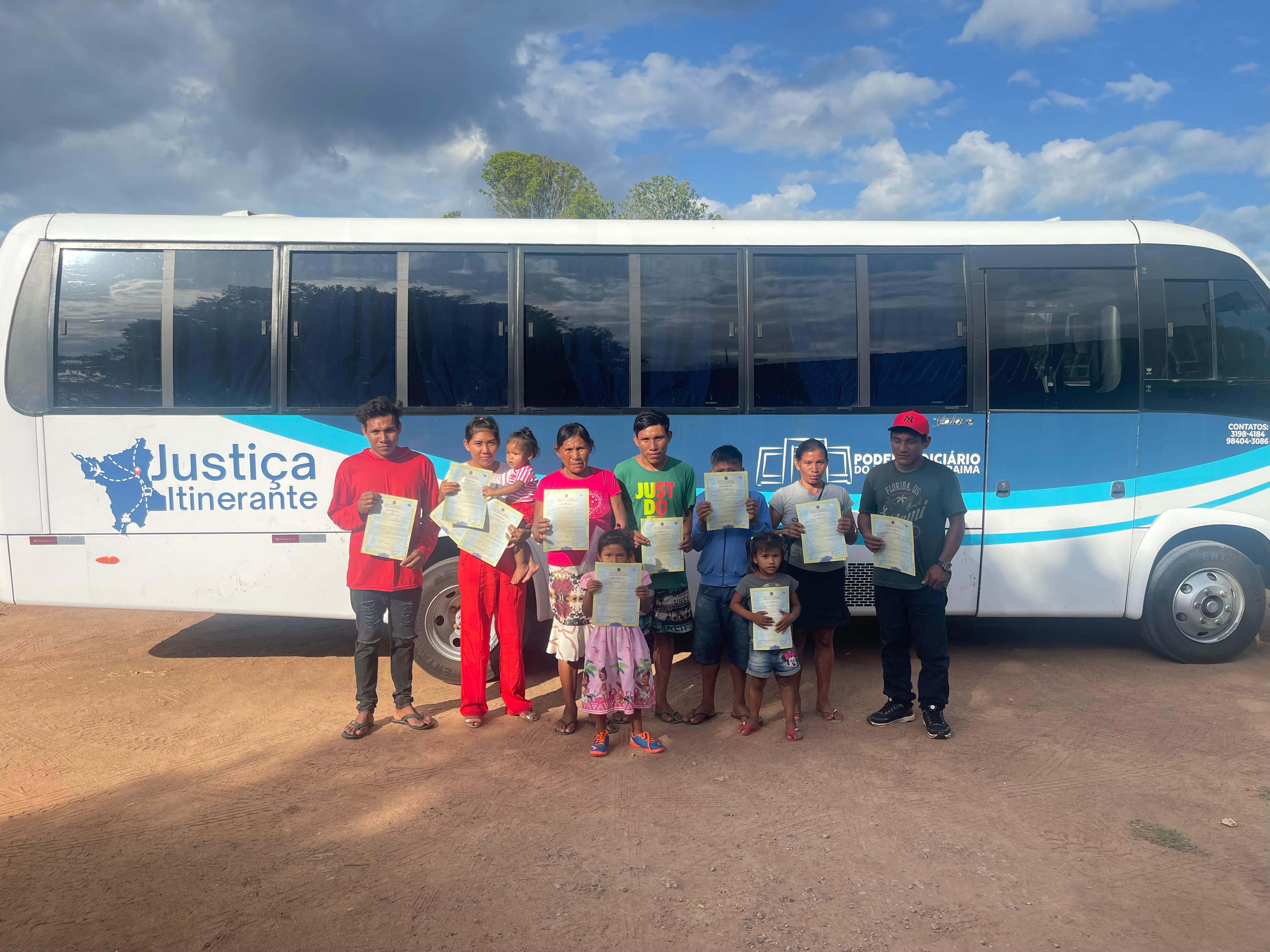 Foto colorida mostrando 10 pessoas, entre crianças, adultos e idosos, em frente ao ônibus da Justiça Itinerante, segurando as certidões de nascimento Foto colorida mostrando 10 pessoas, entre crianças, adultos e idosos, em frente ao ônibus da Justiça Itinerante, segurando as certidões de nascimento