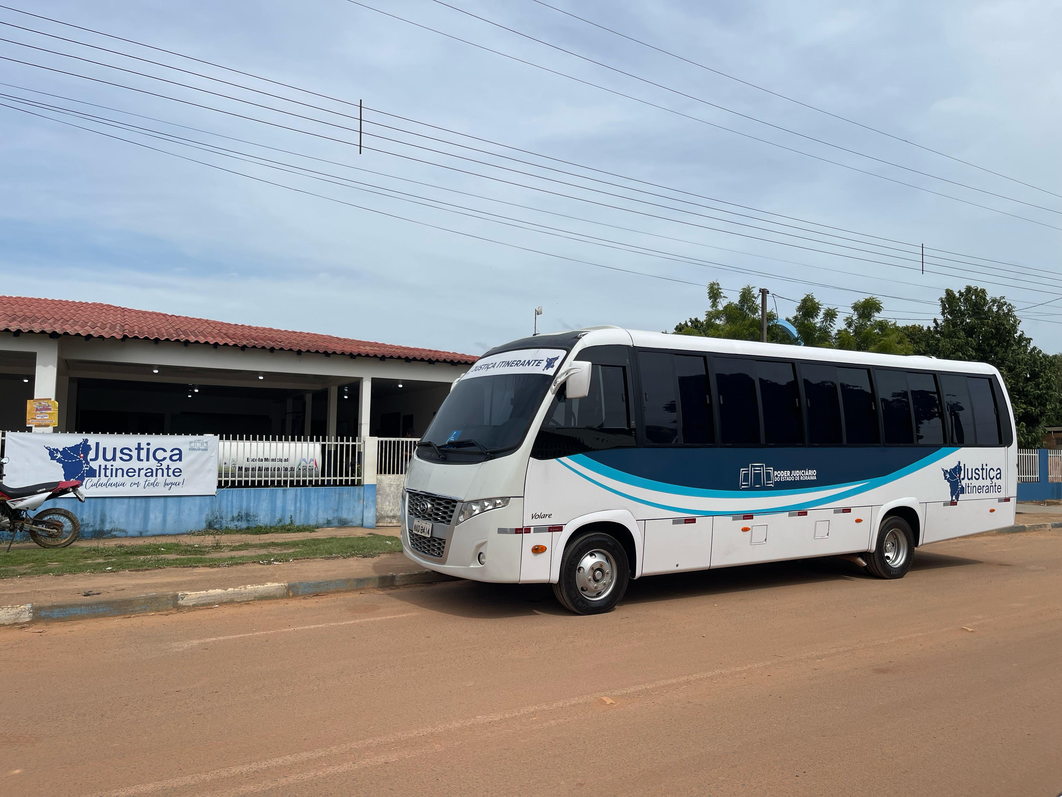 imagem colorida de ônibus adesivado da Vara da Justiça Itinerante em frente à Escola Municipal em Mucajaí, interior do estado de Roraima.