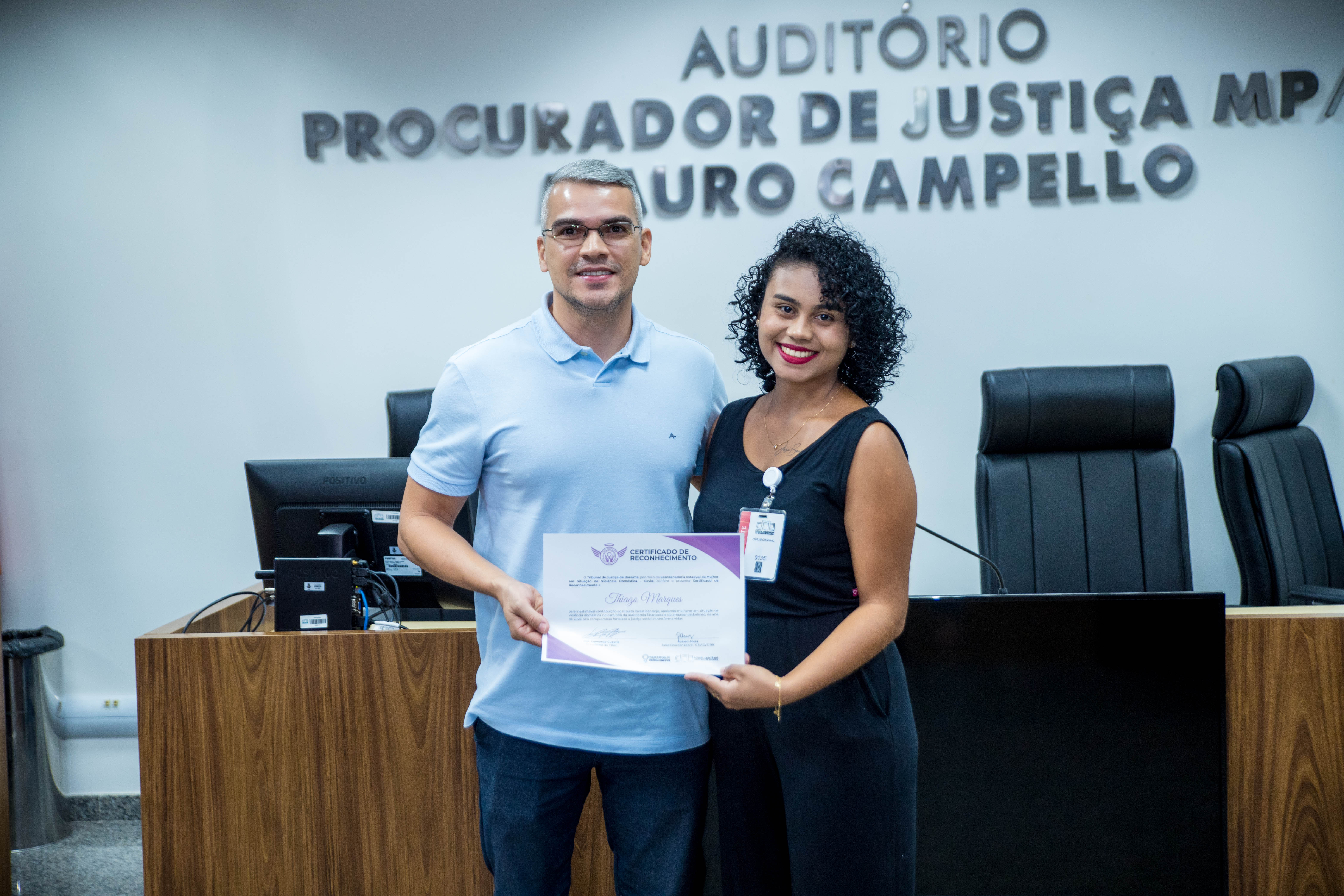 A foto mostra um homem e uma mulher de pé, os dois seguram um certificado. A foto mostra um homem e uma mulher de pé, os dois seguram um certificado.