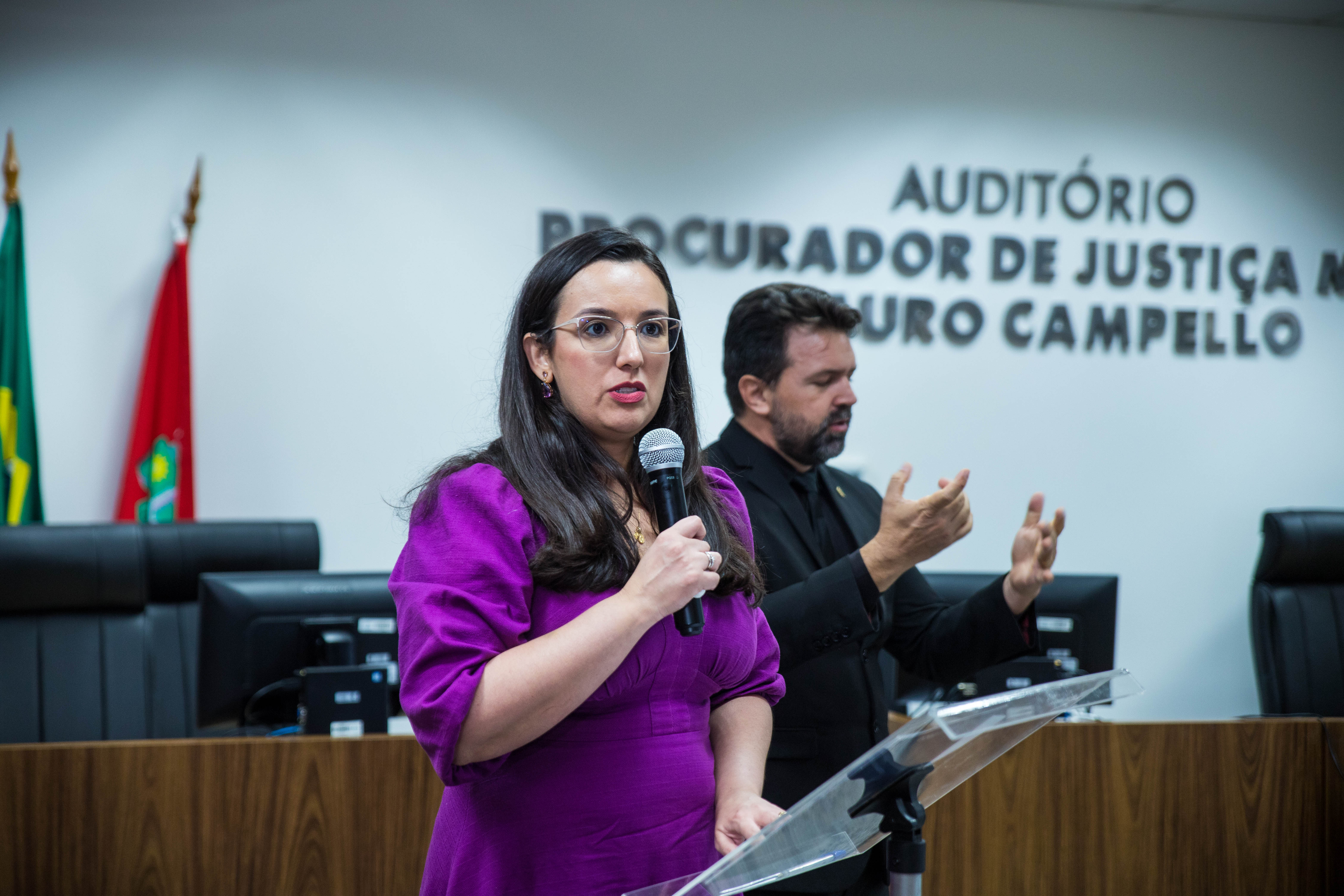 Foto colorida mostrando a Coordenadora Estadual da Mulher em Situação de Violência Doméstica e Familiar do Tribunal de Justiça de Roraima, Juíza Suelen Alves discrusando. Foto colorida mostrando a Coordenadora Estadual da Mulher em Situação de Violência Doméstica e Familiar do Tribunal de Justiça de Roraima, Juíza Suelen Alves discrusando.
