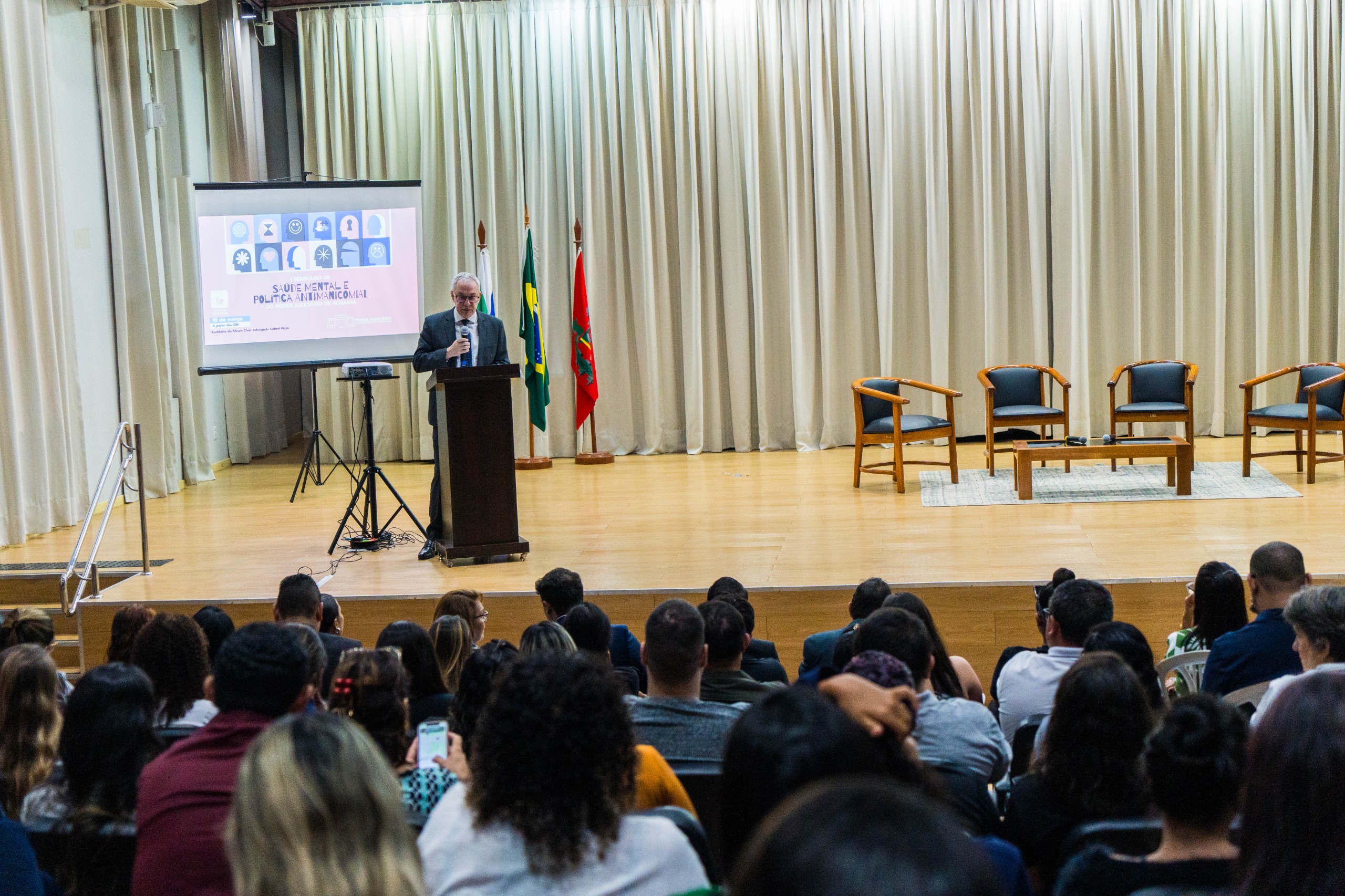 Foto colorida mostra o Desembargador Almiro Padilha discursando em cima do palco do auditório. Mais a frente o publico assiste ao discruso. Foto colorida mostra o Desembargador Almiro Padilha discursando em cima do palco do auditório. Mais a frente o publico assiste ao discruso.