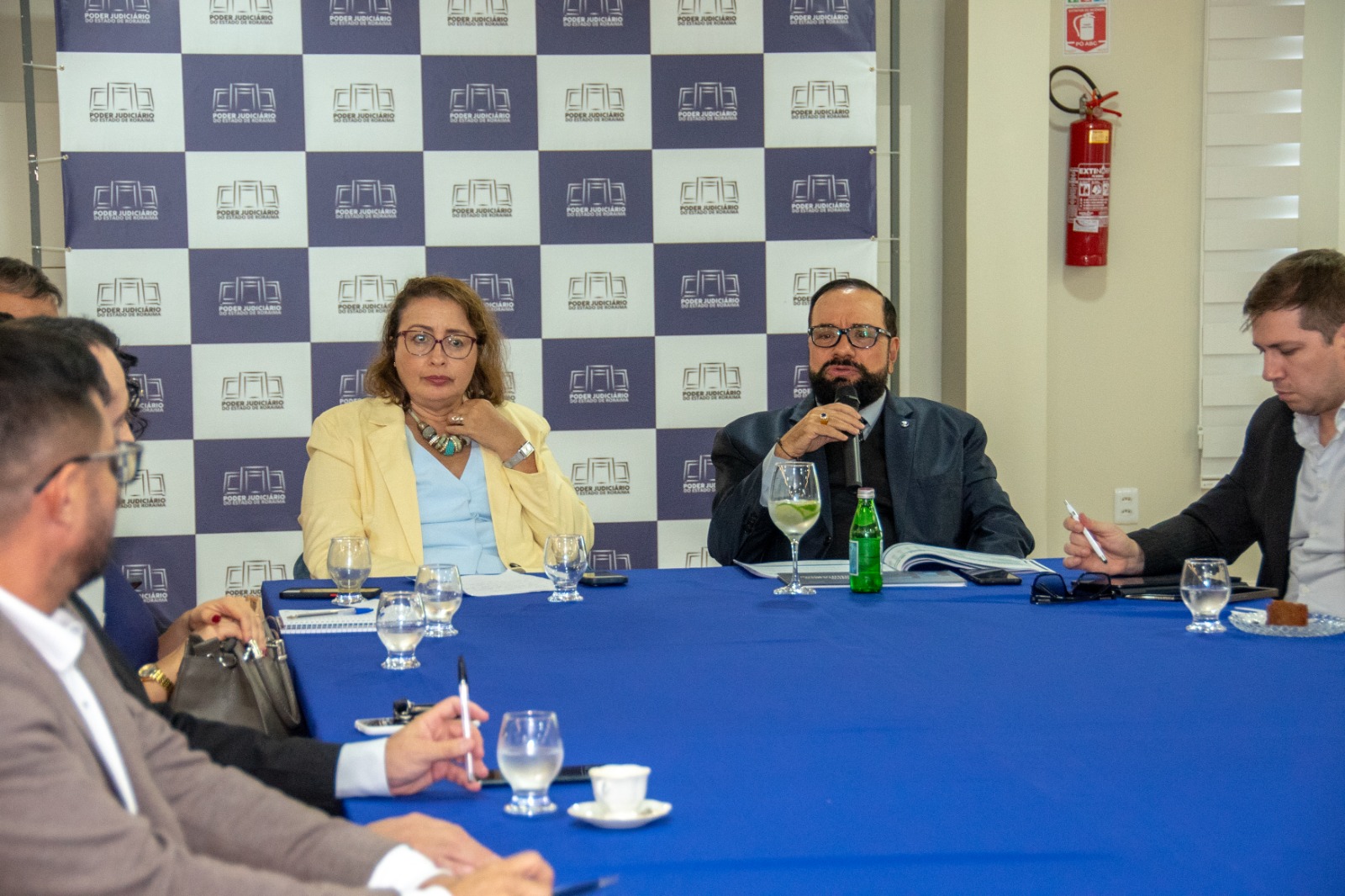 Foto colorida mostra o Desembargador Presidente do TJRR, Leonardo Cupello, discursando. Ele está sentado a frente de uma mesa. Ao seu lado a juiza auxiliar da presidência, Lana Leitão, além de secretários e coordenadores do TJRR Foto colorida mostra o Desembargador Presidente do TJRR, Leonardo Cupello, discursando. Ele está sentado a frente de uma mesa. Ao seu lado a juiza auxiliar da presidência, Lana Leitão, além de secretários e coordenadores do TJRR