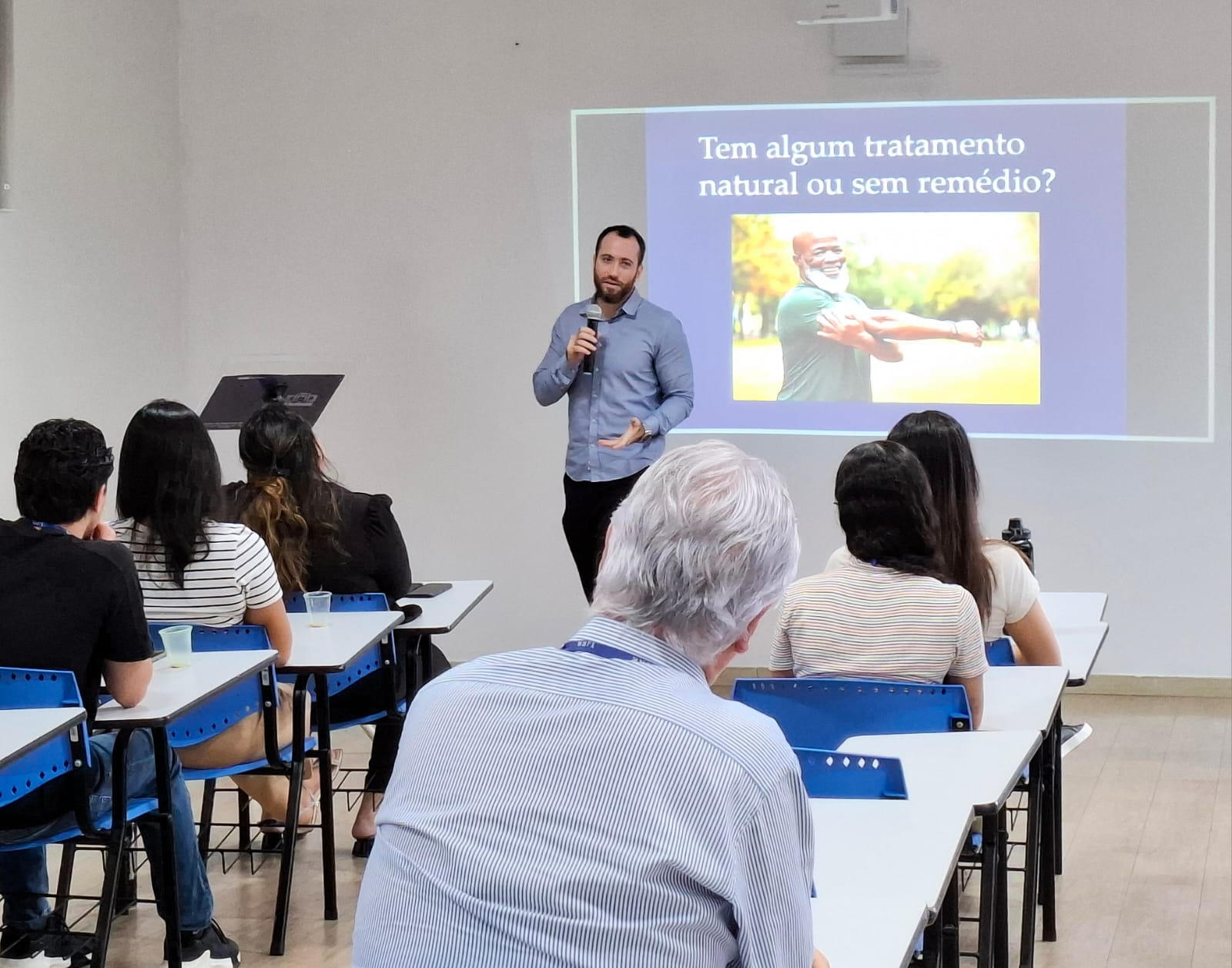 A imagem mostra o secretário de Qualidade de Vida, Dr. Hassan Syagha, palestrando para integrantes do Judiciário roraimense, sentados em filas de cadeiras. O tema da palestra é a hipertensão arterial sistêmica, com foco na prevenção, diagnóstico e tratamento da condição. Ao fundo, pode-se observar uma apresentação de PowerPoint projetada na parede, com a pergunta: “Tem algum tratamento natural ou sem remédio?” A imagem mostra o secretário de Qualidade de Vida, Dr. Hassan Syagha, palestrando para integrantes do Judiciário roraimense, sentados em filas de cadeiras. O tema da palestra é a hipertensão arterial sistêmica, com foco na prevenção, diagnóstico e tratamento da condição. Ao fundo, pode-se observar uma apresentação de PowerPoint projetada na parede, com a pergunta: “Tem algum tratamento natural ou sem remédio?”
