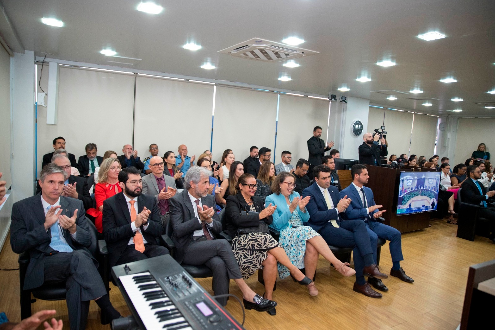 Foto colorida mostra o publico presente que está acompanhando a sessão solene. Além das pessoas sentadas na poltrona, ao fundo, há um interprete de libras.