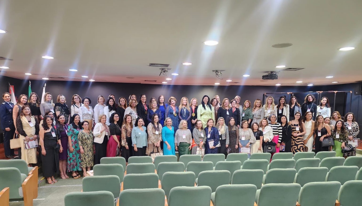 Foto colorida mostrando 62 pessoas em pé posando para foto em um auditório   