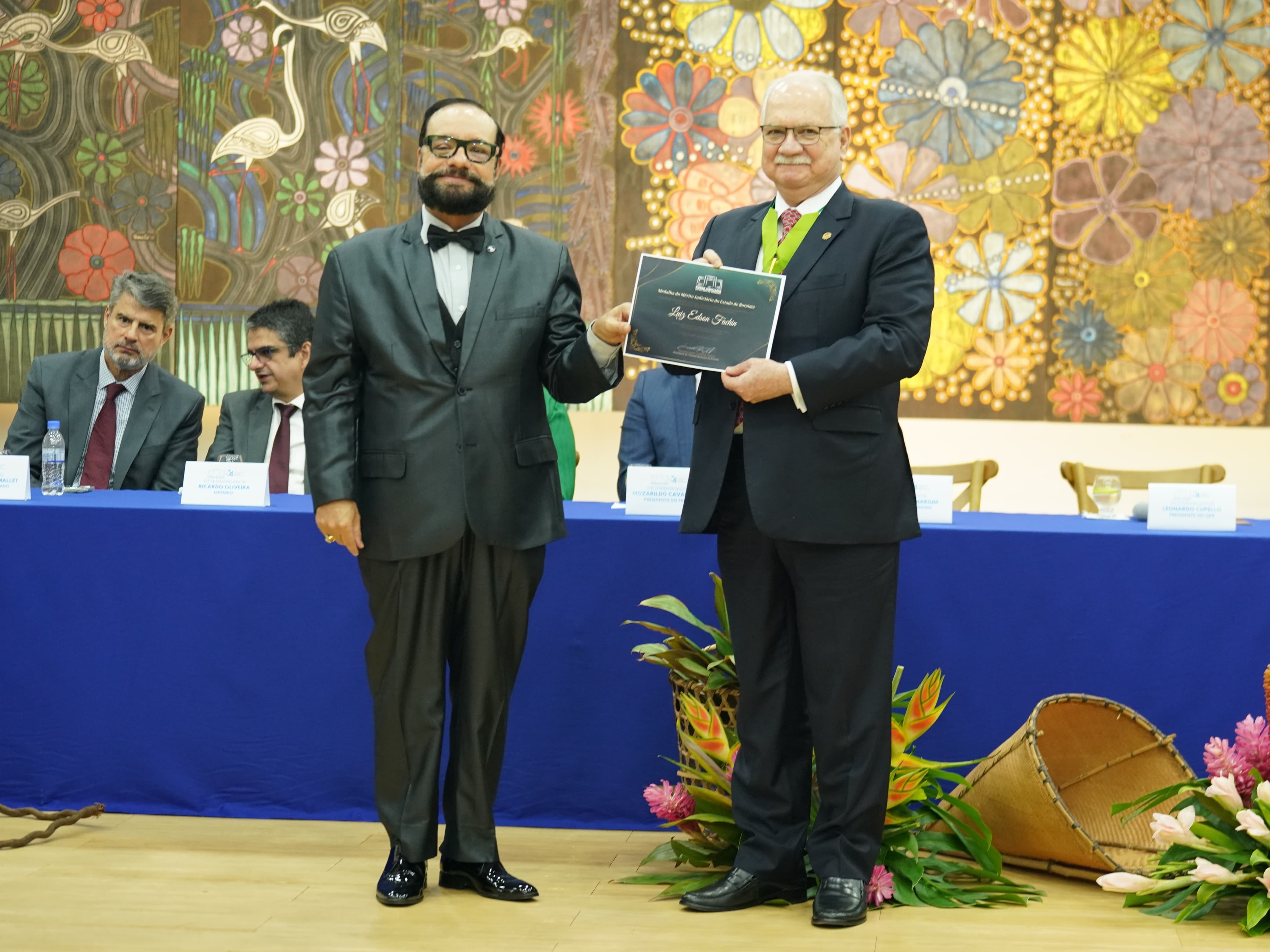 Foto colorida mostra o presidente do TJRR, desembargador Leonardo Cupello, posando para fotografia ao lado do ministro do STF, Edson Fachin. O ministro segura o certificado da Medalha do Mérito Judiciário do Estado de Roraima. Ao fundo, vê-se a mesa de autoridades. Foto colorida mostra o presidente do TJRR, desembargador Leonardo Cupello, posando para fotografia ao lado do ministro do STF, Edson Fachin. O ministro segura o certificado da Medalha do Mérito Judiciário do Estado de Roraima. Ao fundo, vê-se a mesa de autoridades.