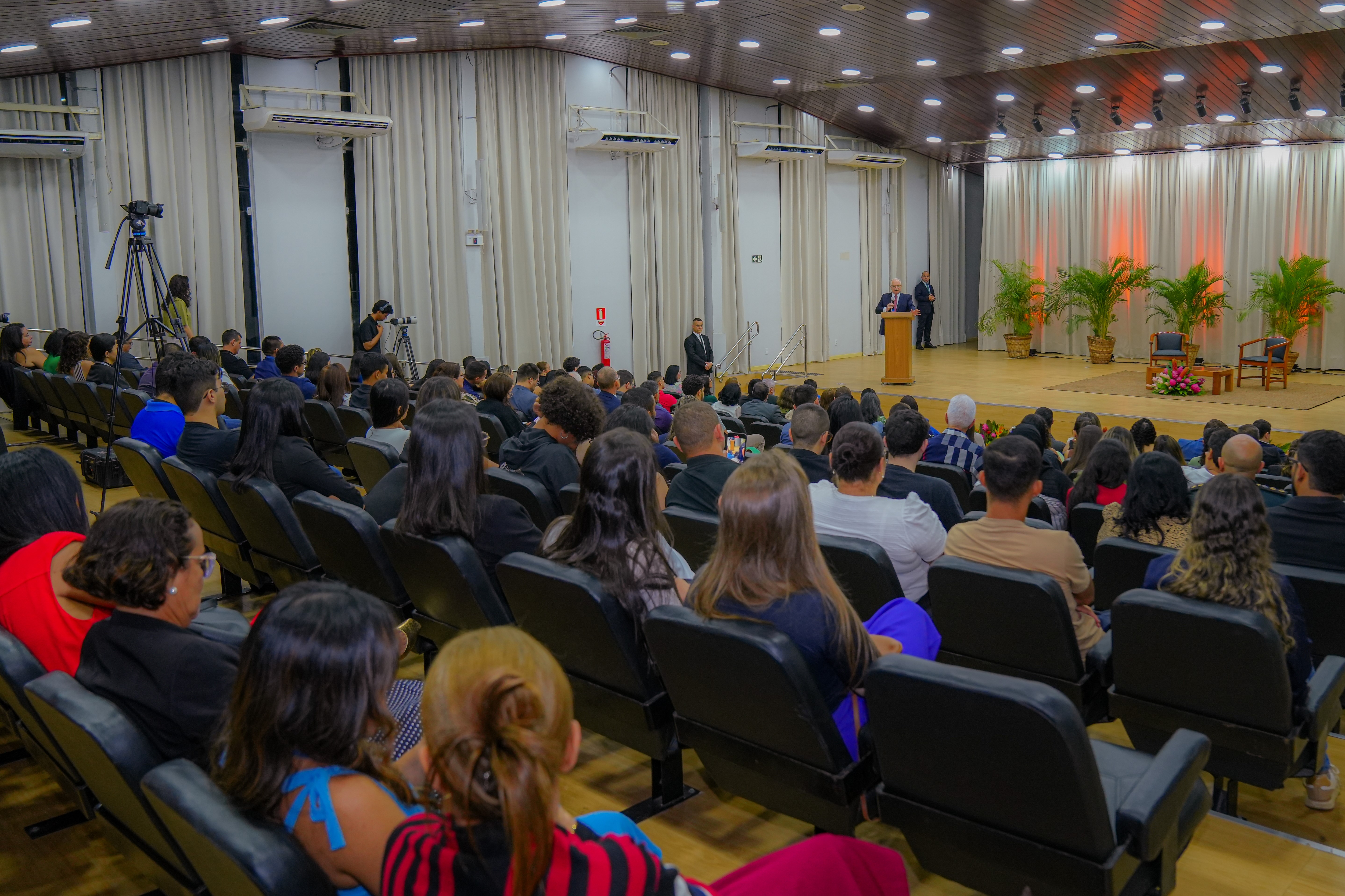 A imagem mostra o Ministro Edson Fachin discursando em um auditório, em pé atrás de um púlpito no centro do palco. A plateia, vista de costas, assiste atenta. O ambiente é formal, com cortinas claras e iluminação suave. A imagem mostra o Ministro Edson Fachin discursando em um auditório, em pé atrás de um púlpito no centro do palco. A plateia, vista de costas, assiste atenta. O ambiente é formal, com cortinas claras e iluminação suave.