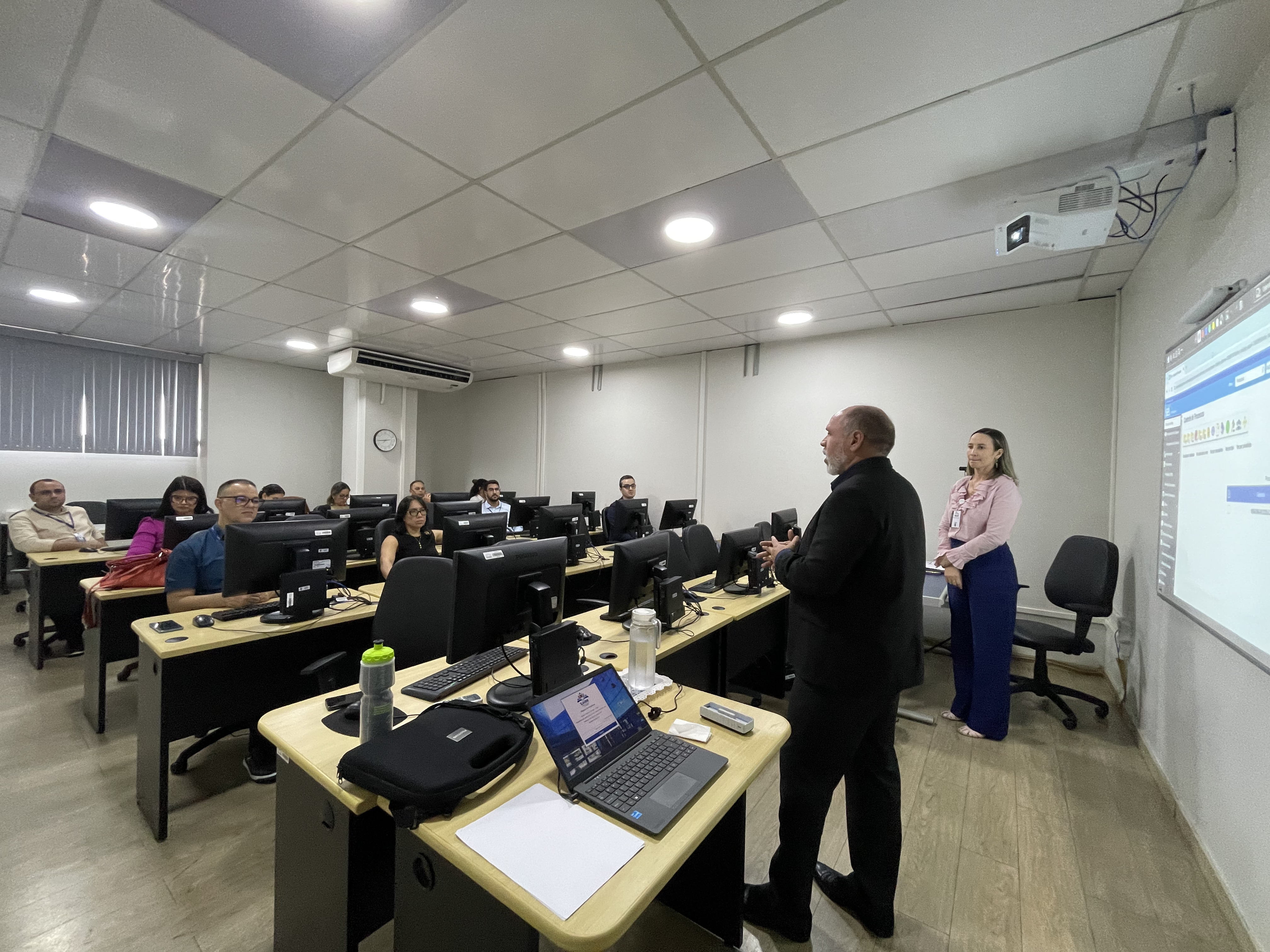 Imagem colorida de uma sala composta por um grupo de pessoas sentado à mesa com computadores individuais em fileiras e afrente o Secretário de Tecnologia e Informação do TJRR, Sormany Brilhante, falando ao lado da instrutora Imagem colorida de uma sala composta por um grupo de pessoas sentado à mesa com computadores individuais em fileiras e afrente o Secretário de Tecnologia e Informação do TJRR, Sormany Brilhante, falando ao lado da instrutora