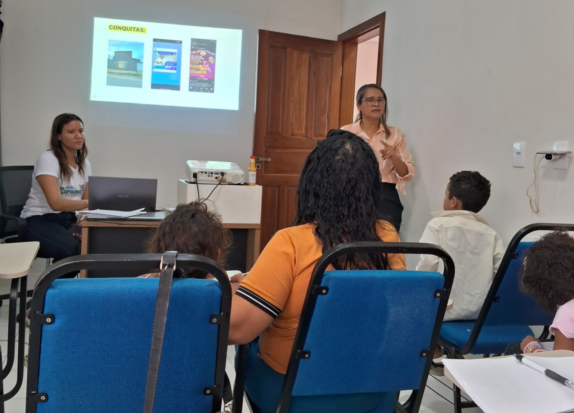  Imagem colorida mostra seis pessoas em uma sala de aula. Duas estão de pé, à frente, repassando orientações, enquanto as demais permanecem sentadas, atentas às instruções.