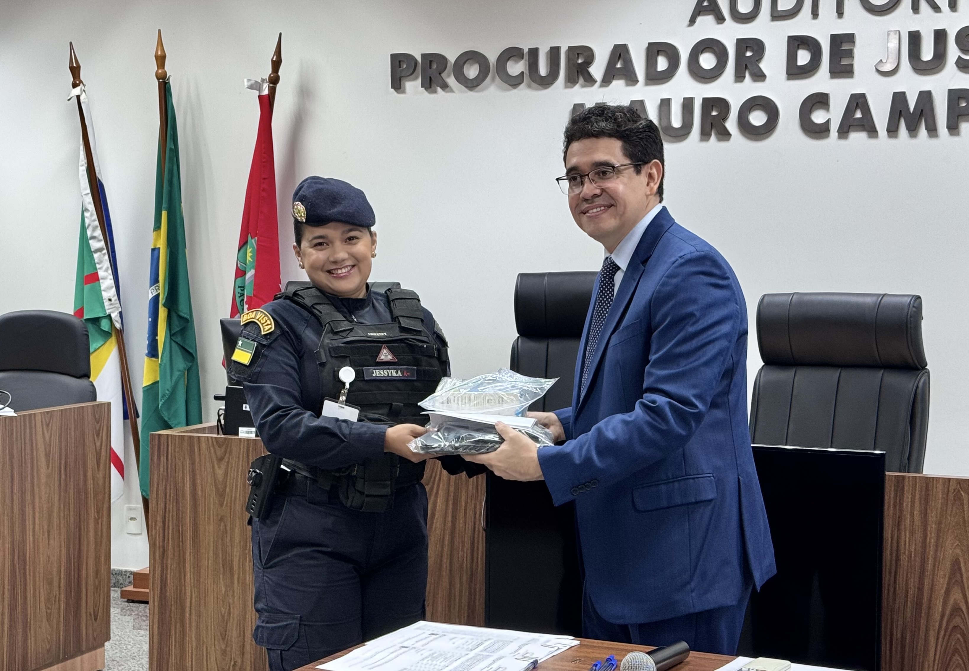 Imagem colorida de um homem entregando um saco transparente contendo os itens doados a uma representante da Patrulha Maria da Penha. Imagem colorida de um homem entregando um saco transparente contendo os itens doados a uma representante da Patrulha Maria da Penha.
